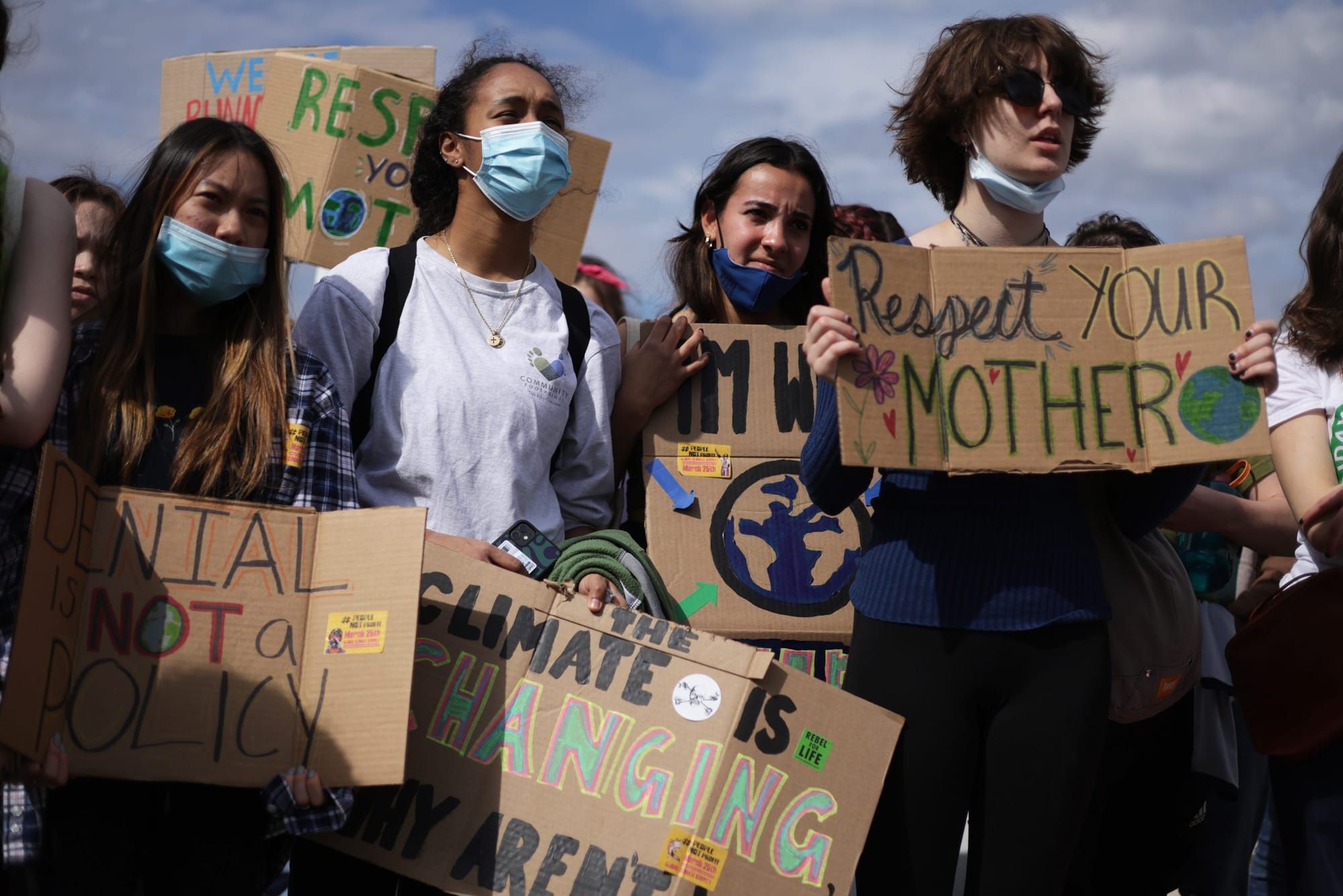 color photograph of a youth climate protest. several youths wearing masks hold brown cardboard signs with slogans like "respe
