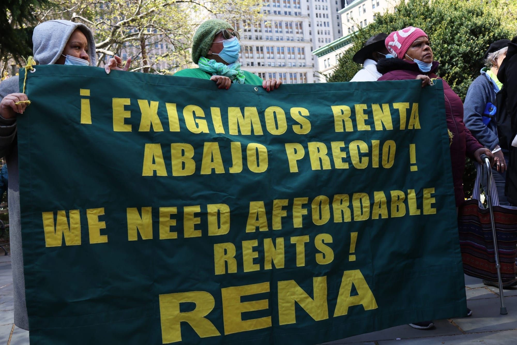 color photograph of masked protesters holding a large dark green cloth banner with yellow sans serif text reading: "exigimos