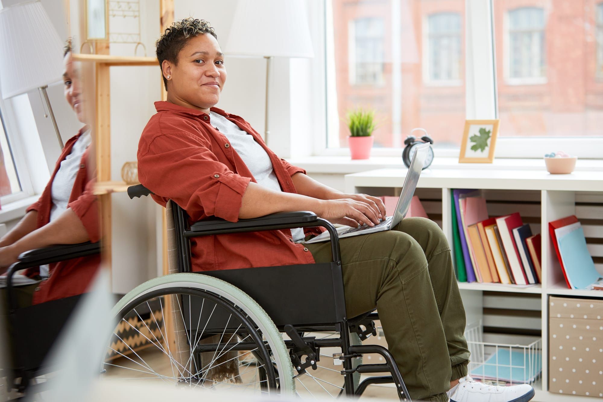 photo of a disabled person with light brown skin and curly short hair sitting in wheelchair and looking at camera while using