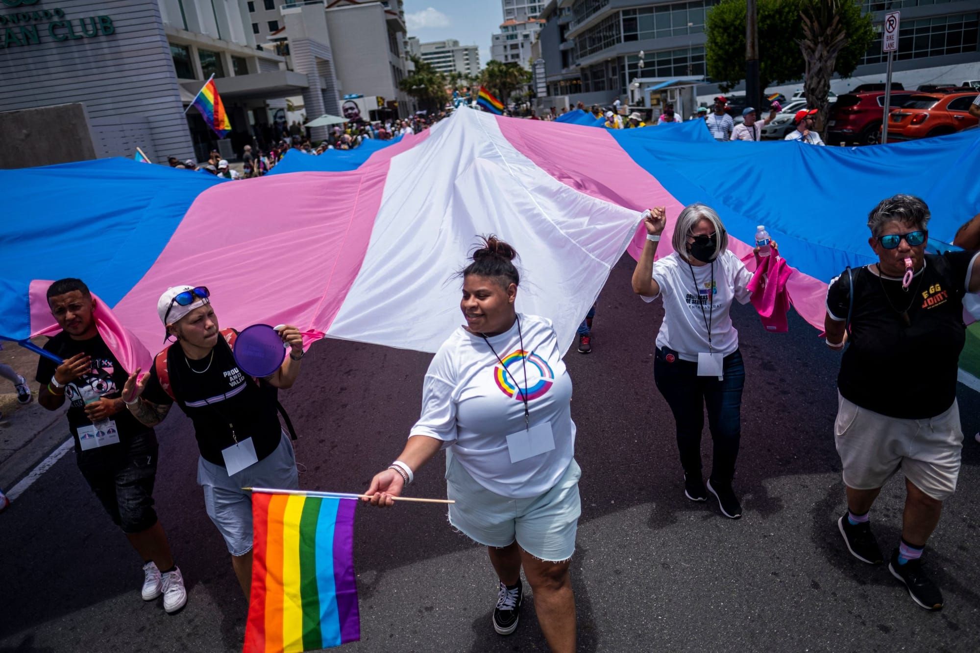 color photograph of a 2022 Pride celebration in Puerto Rico. Several people hold the edges of an enormous trans Pride flag. t