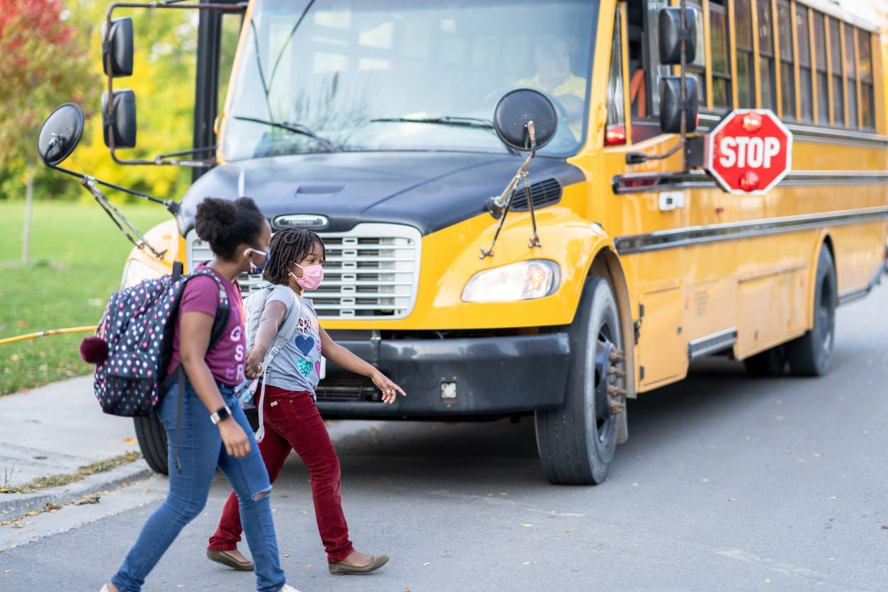color photograph of two young girls crossing the road to get to their bus. They are dressed casually and each have a backpack