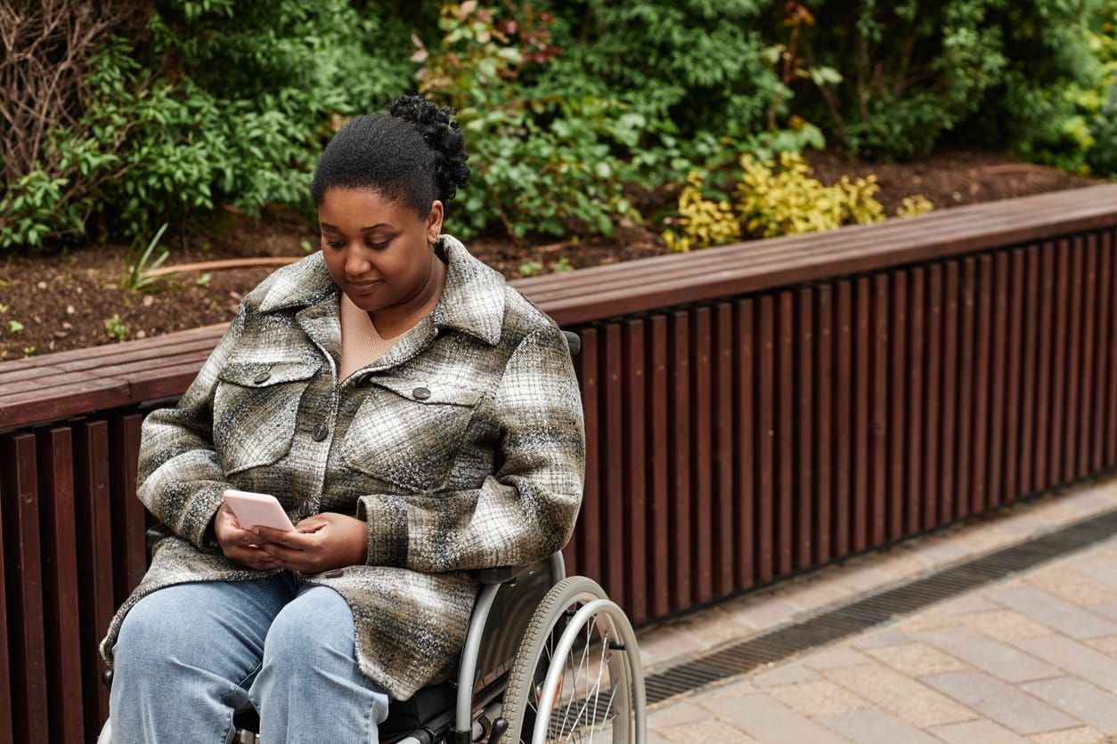 color photograph stock image of a black woman in a white and grey jacket and light blue jeans sitting in a wheelchair looking
