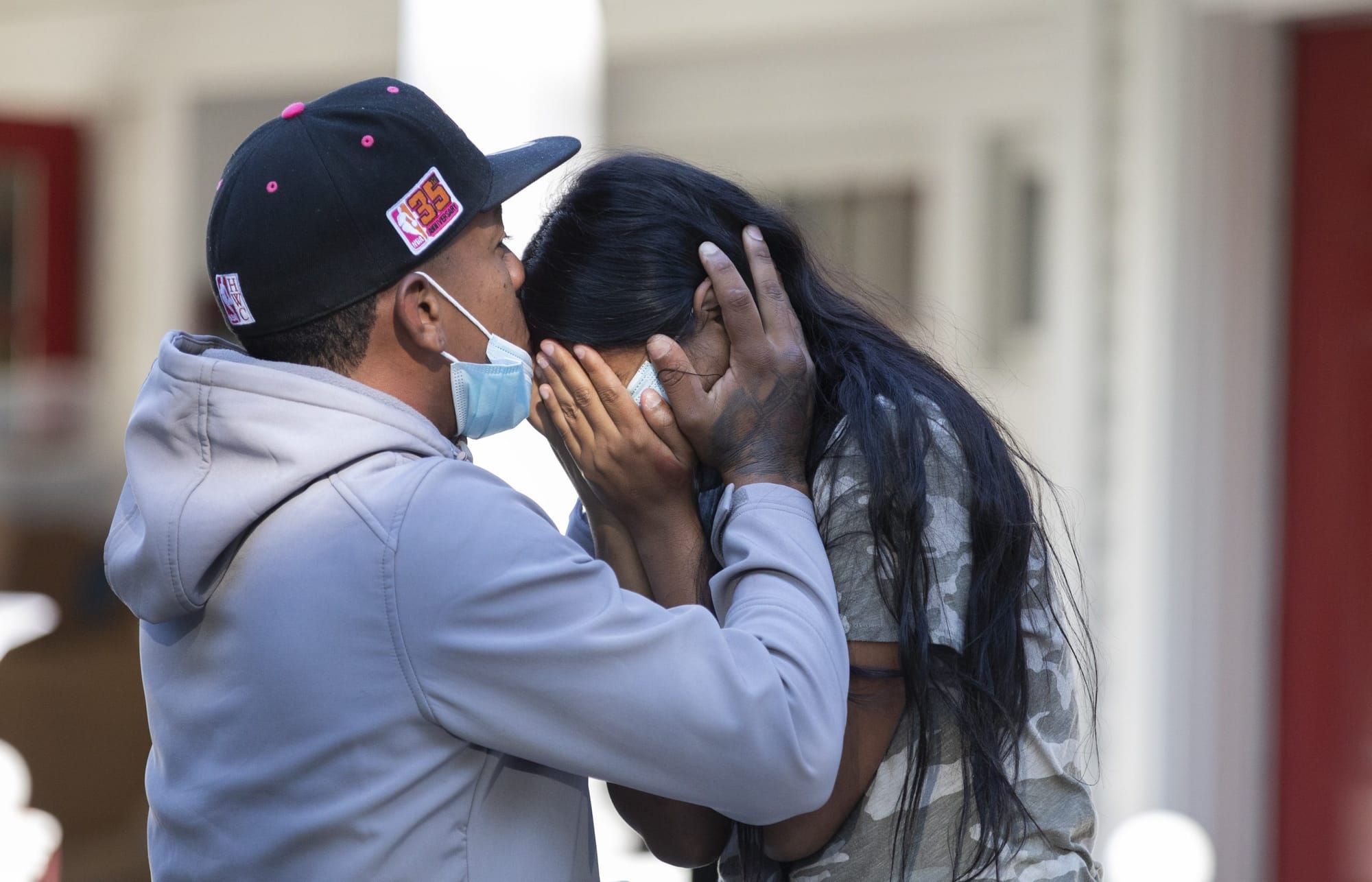 color photograph of two Black undocumented immigrants. one, wearing a grey sweatshirt and a baseball cap over short hair, hol