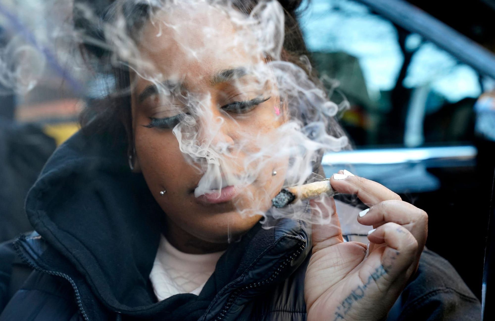 color photograph close-up of a black woman exhaling marijuana smoke towards the camera