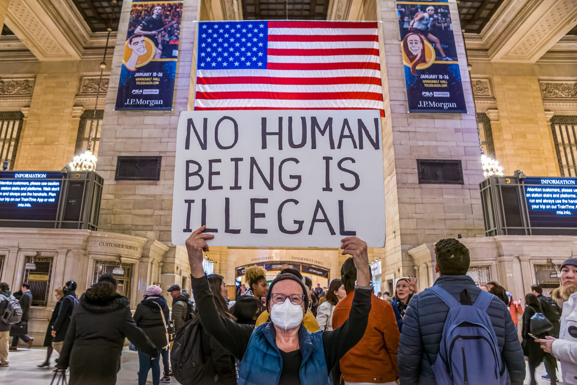 color photograph of an indoor protest in Grand Central Station in New York City. a person in the foreground wears a mask and