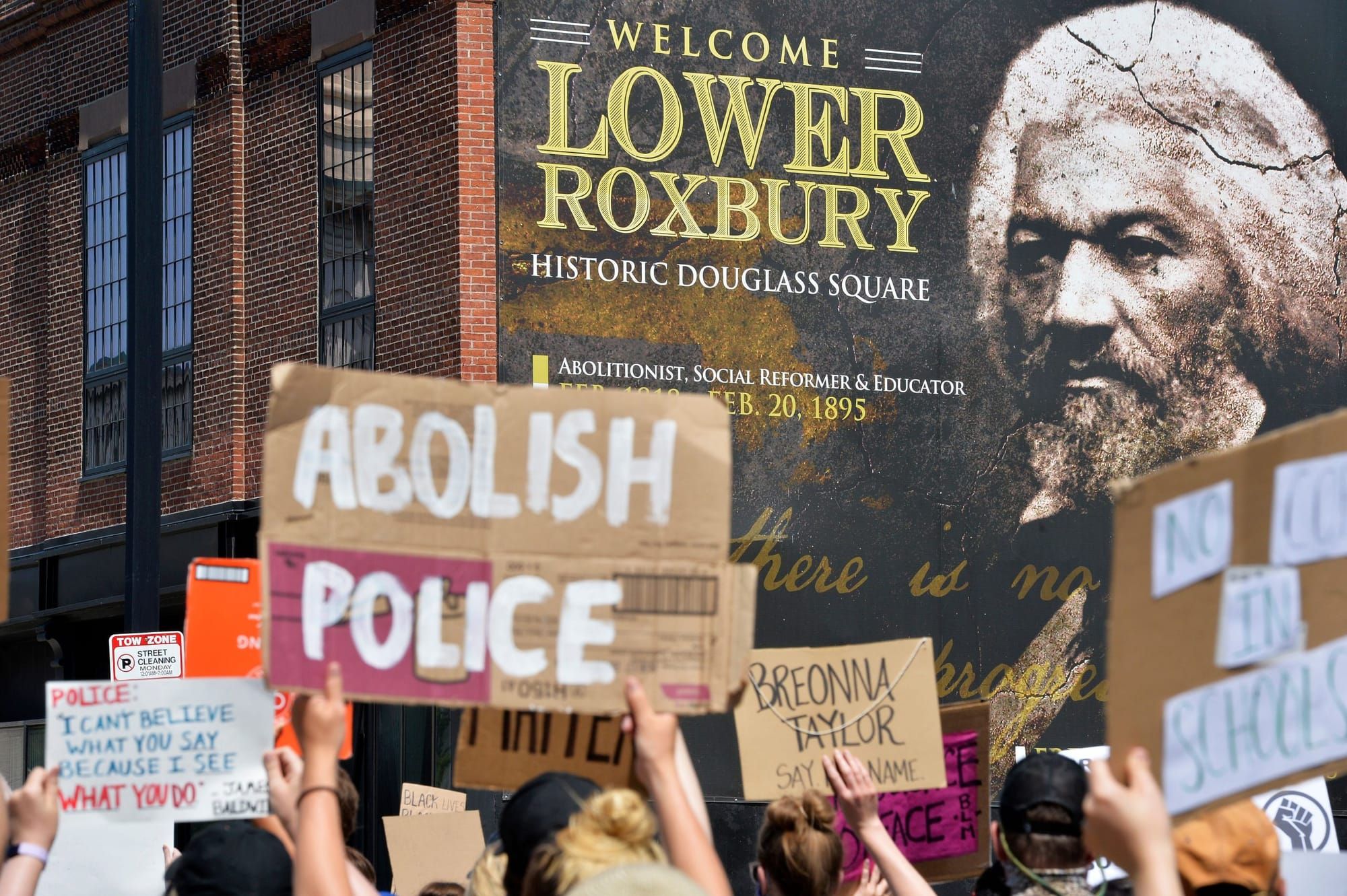color photograph of an outdoor protest against police. people hold up cardboard signs reading "abolish police" in the foregro