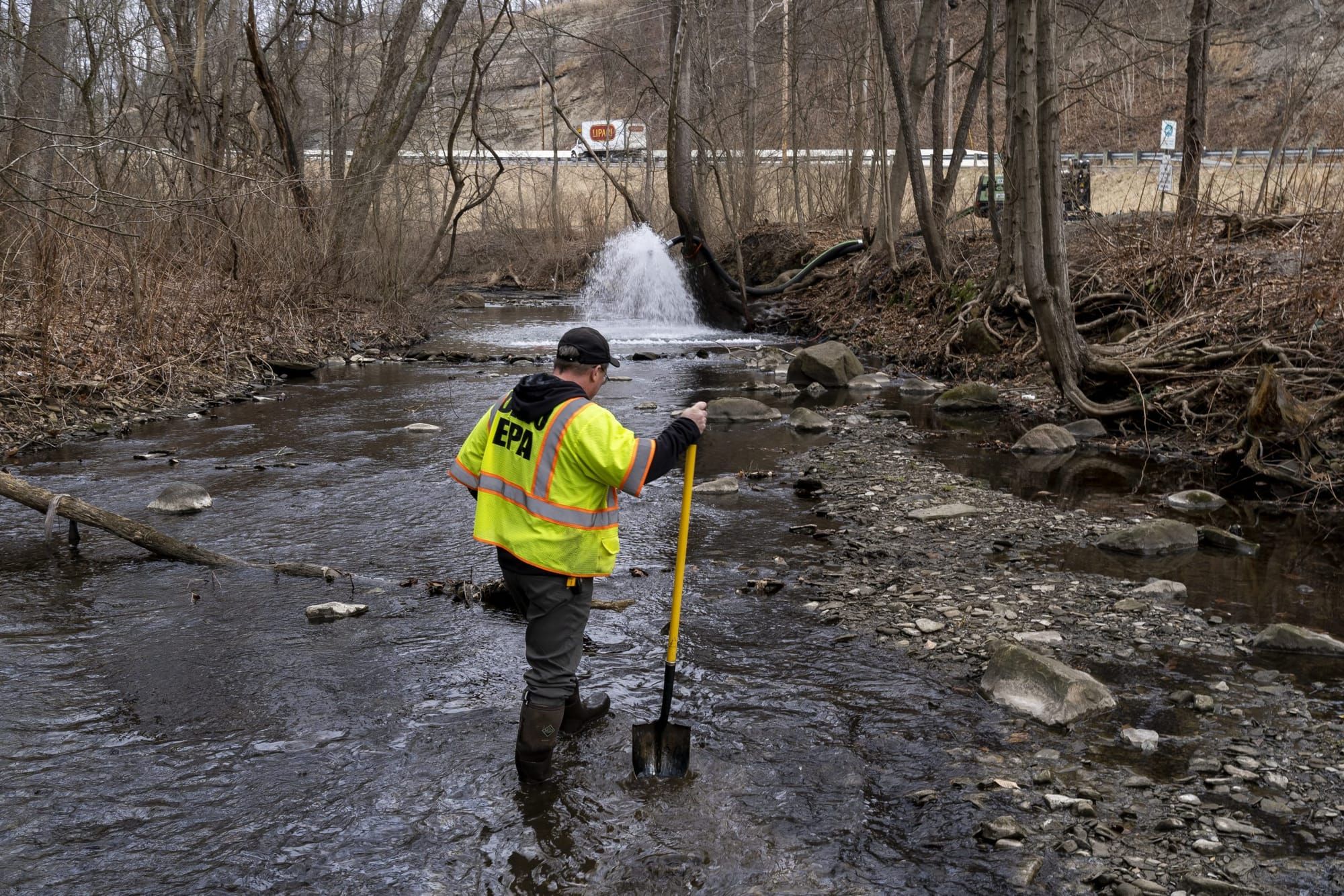 color photograph of an EPA agent wearing a bright yellow safety vest standing in a creek