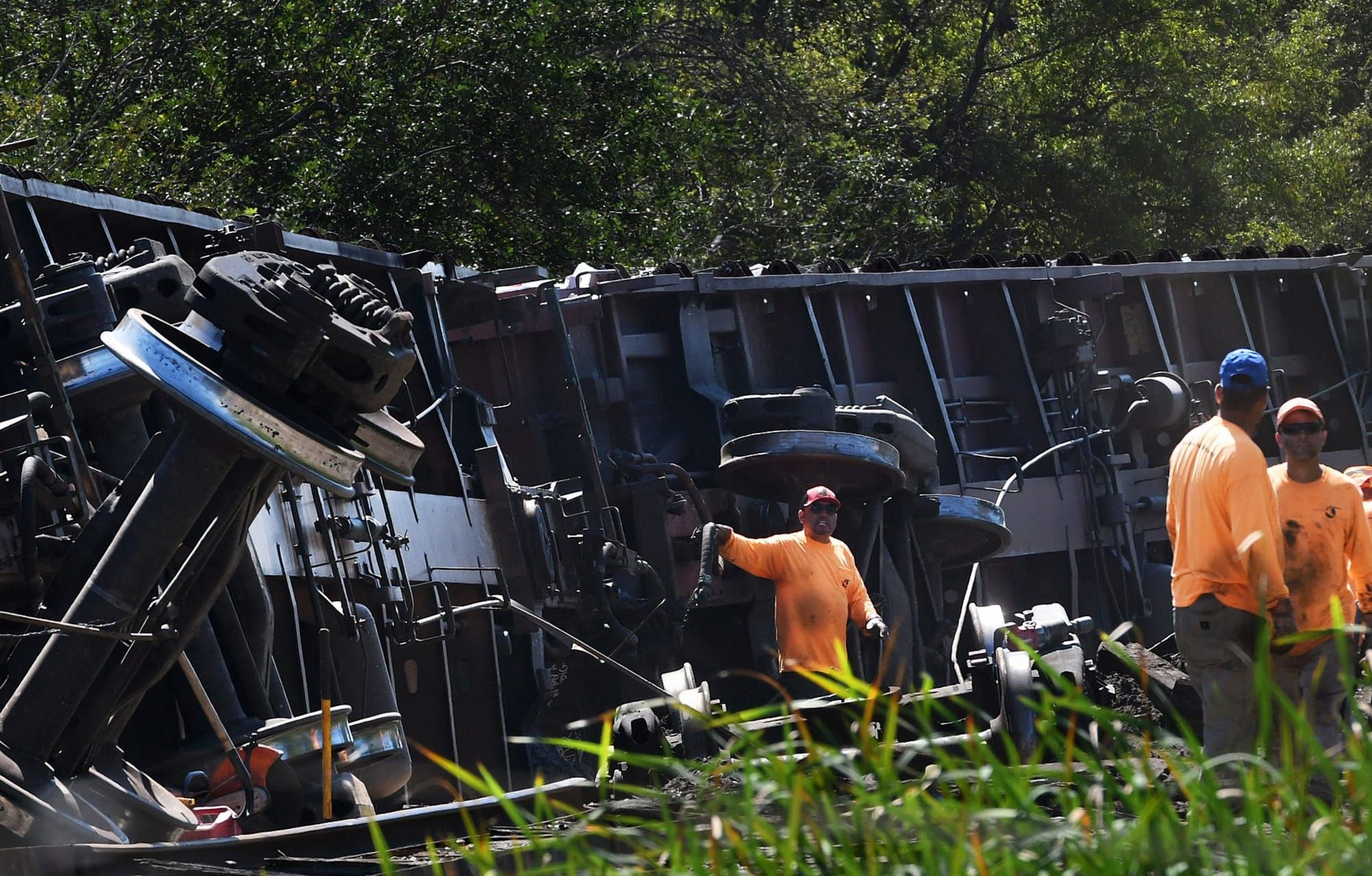 color photograph of three train workers standing near a derailed train