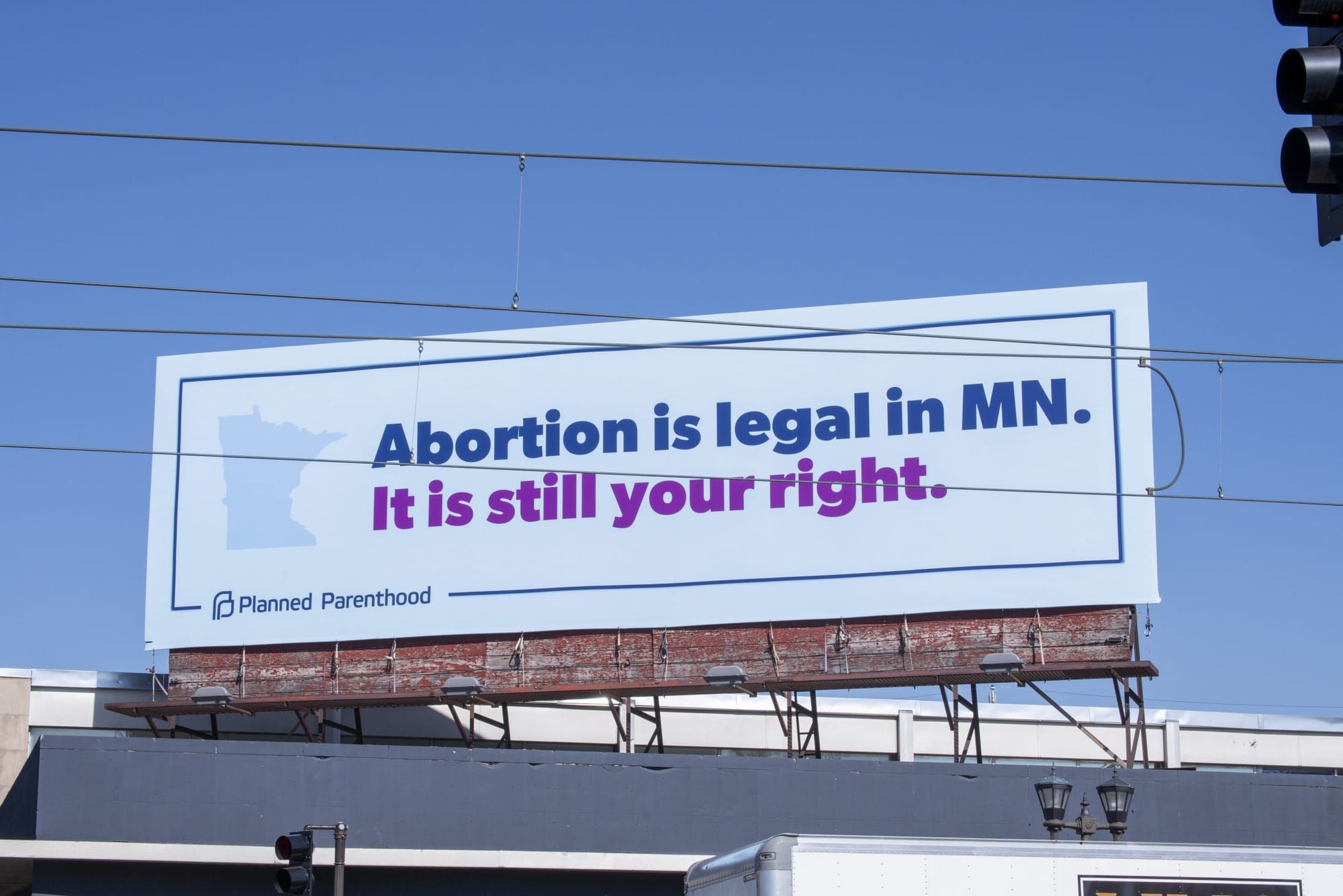 color photograph of a planned parenthood ad on a white billboard atop a building roof that reads "abortion is legal in MN" in