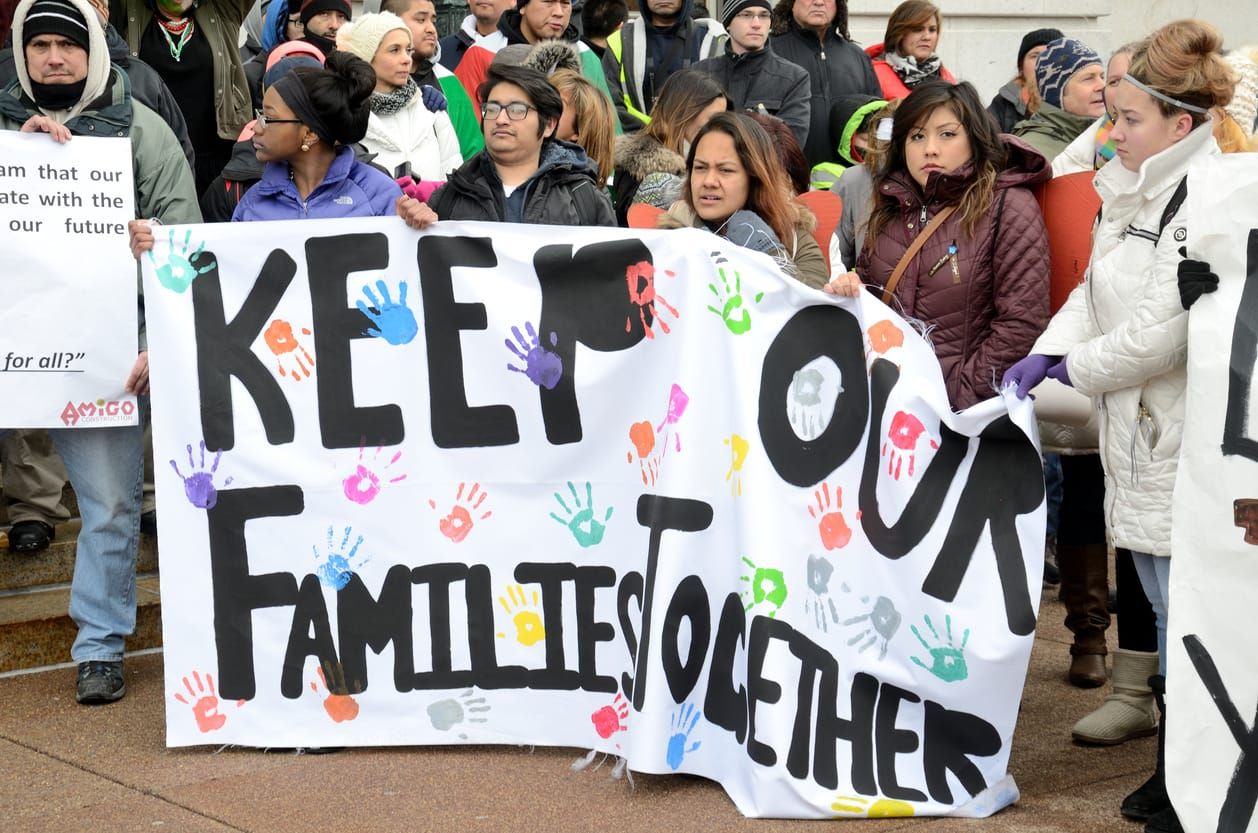 color stock photo of an immigrant rights protest. five people hold a long white banner that reads "keep our families together