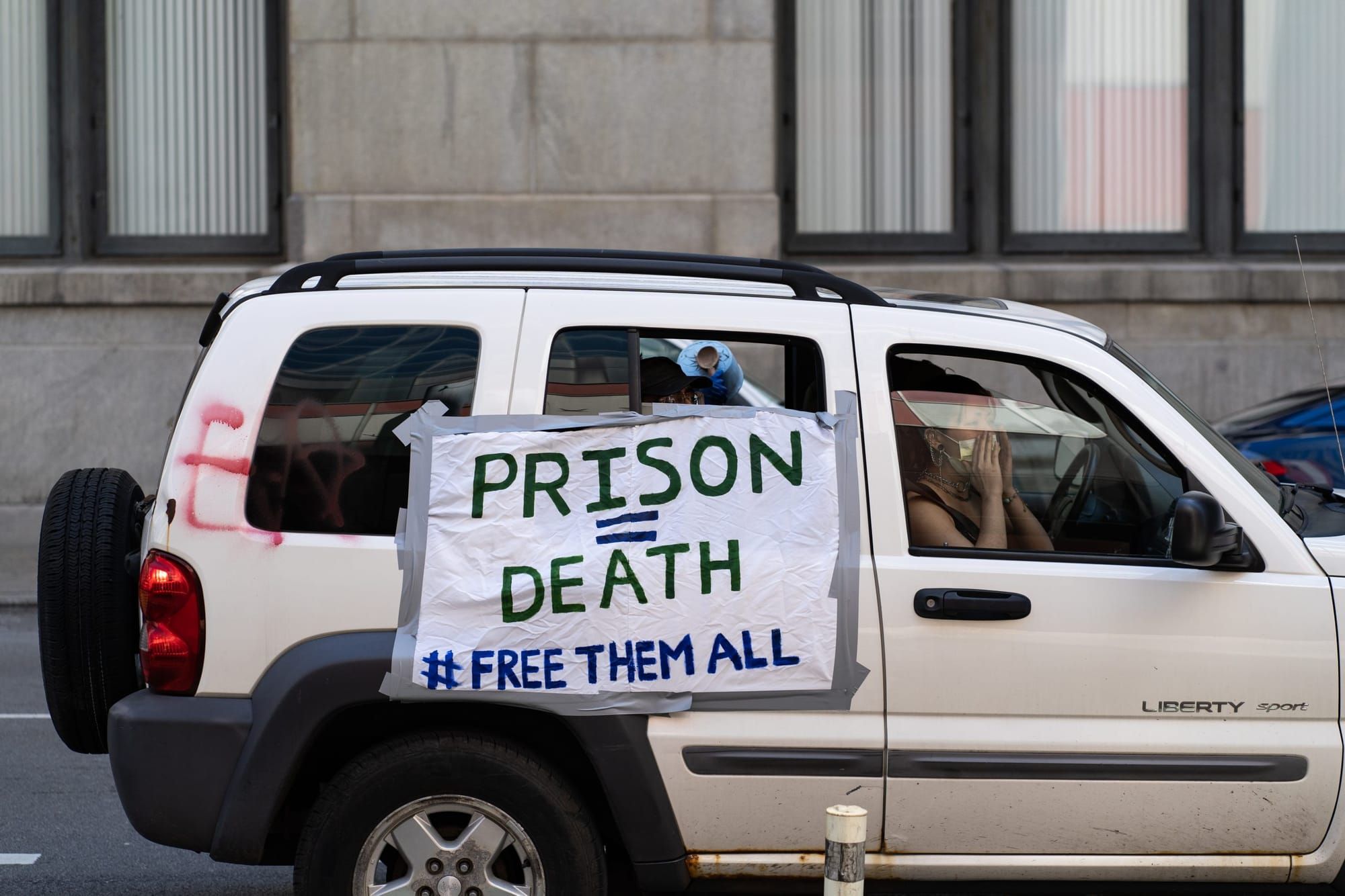 color photograph of a white car from the side. duct taped to the side is a large white paper poster that reads "Prison = Deat