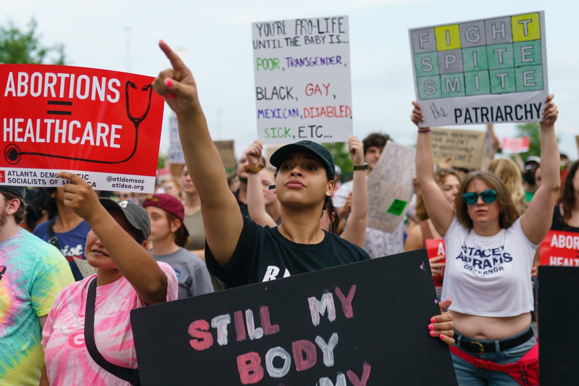 color photograph of an outdoor protest where people hold up signs in support of abortion with slogans like "abortion = health