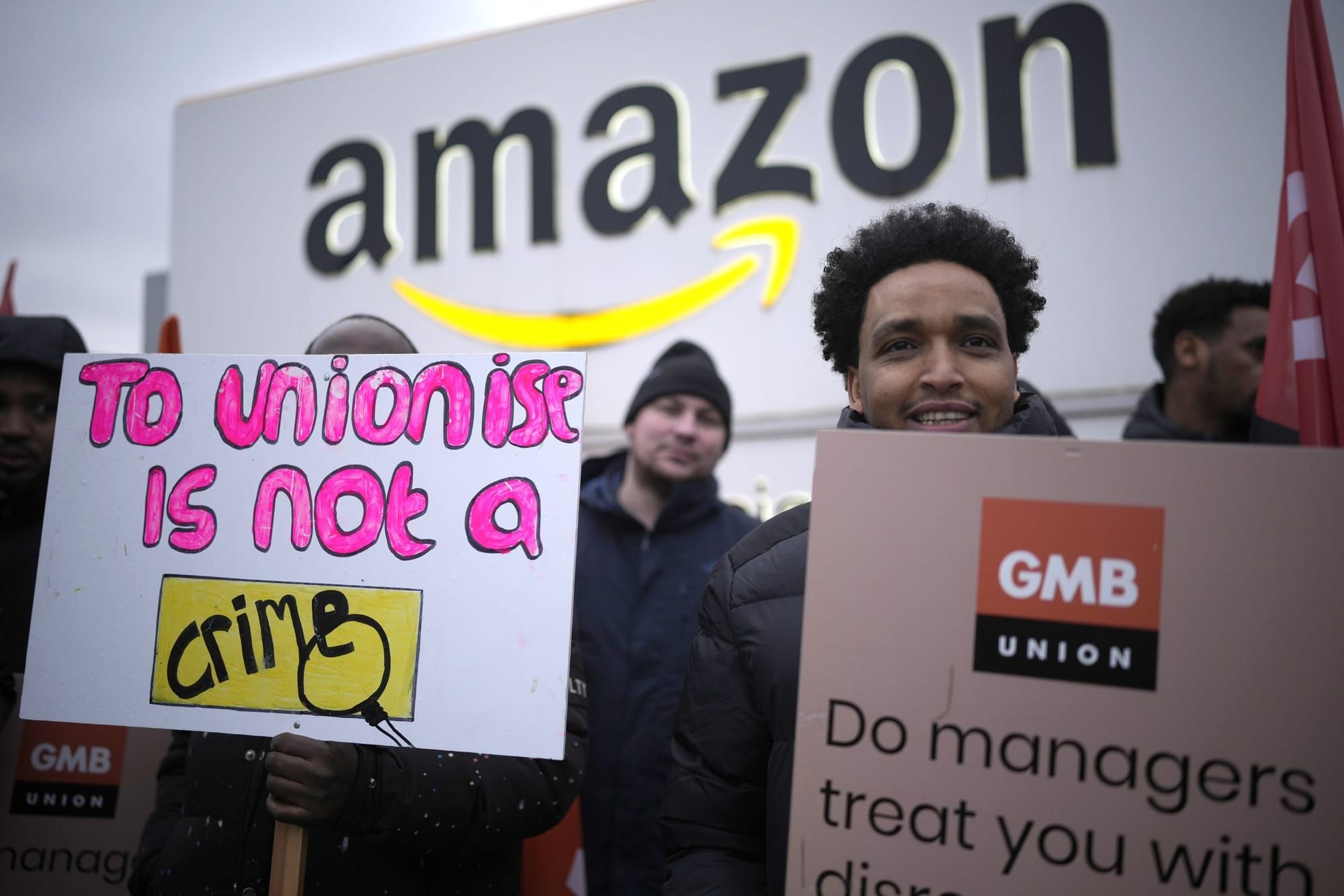 color photograph of an outdoor protest in support of amazon workers unionizing. in the foreground, people hold up signs that