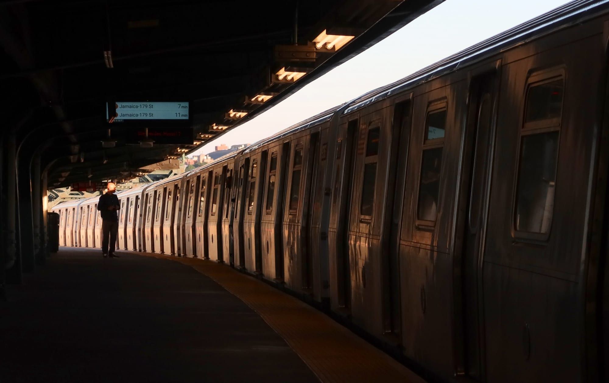 color photograph of a new york subway train passing an outdoor station and blocking out the daylight
