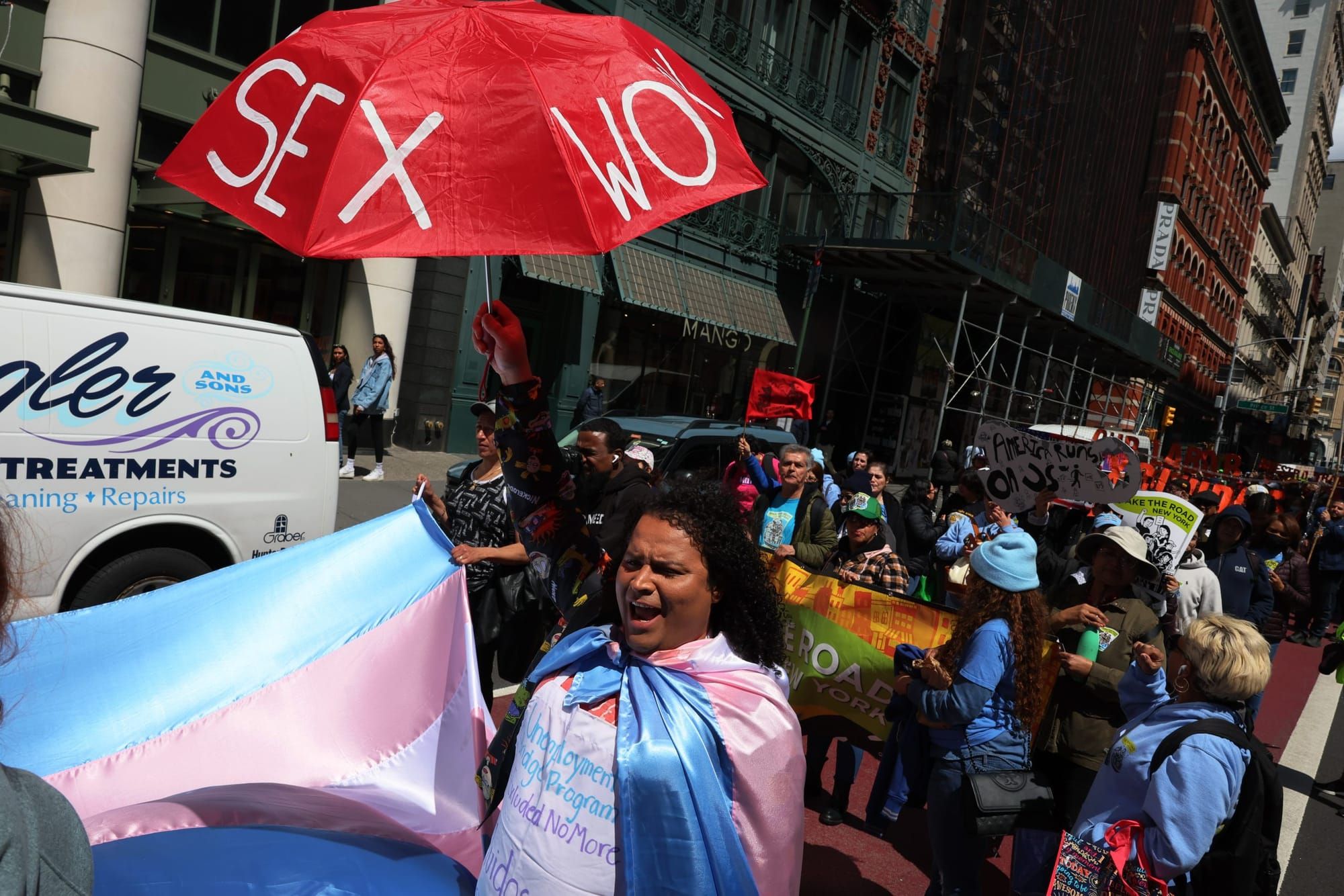 color photograph of an outdoor protest in support of workers' rights. a femme person with shoulder-length curly brown hair ho