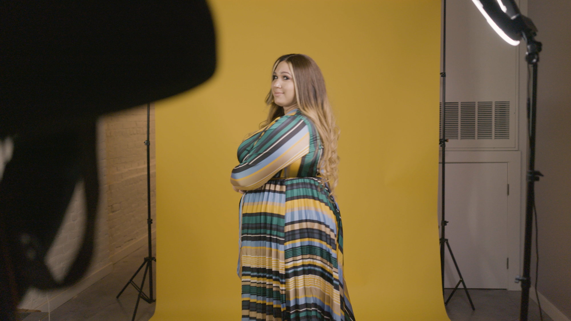 color photograph of a Black trans woman with blonde hair past her shoulders wearing a vertically striped green, black, and ye
