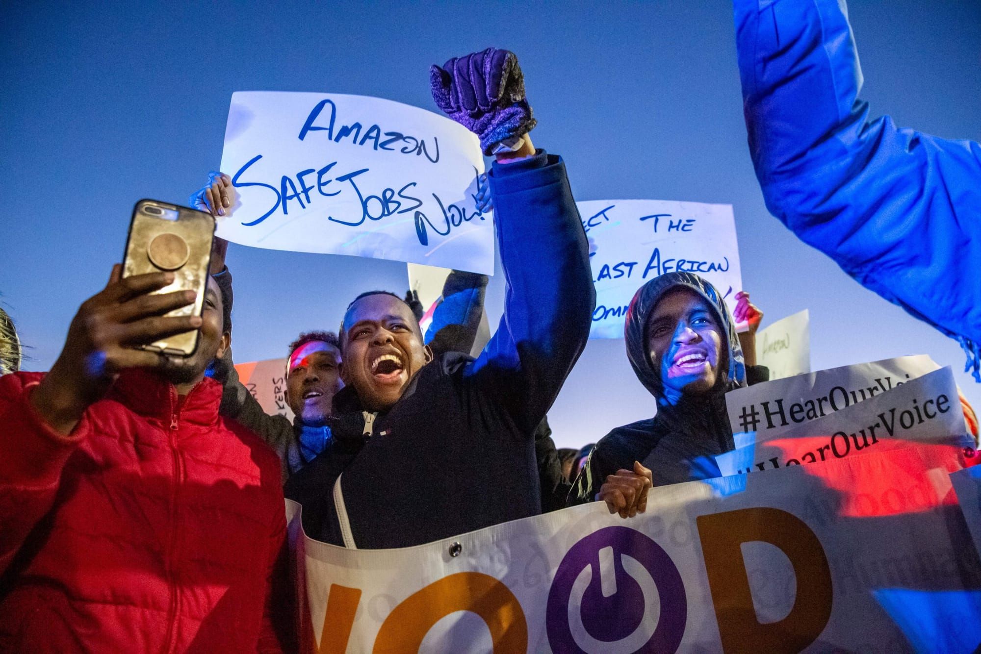 color photograph of an outdoor protest where Somali workers raise their fists and hold signs in support of workers rights. Si