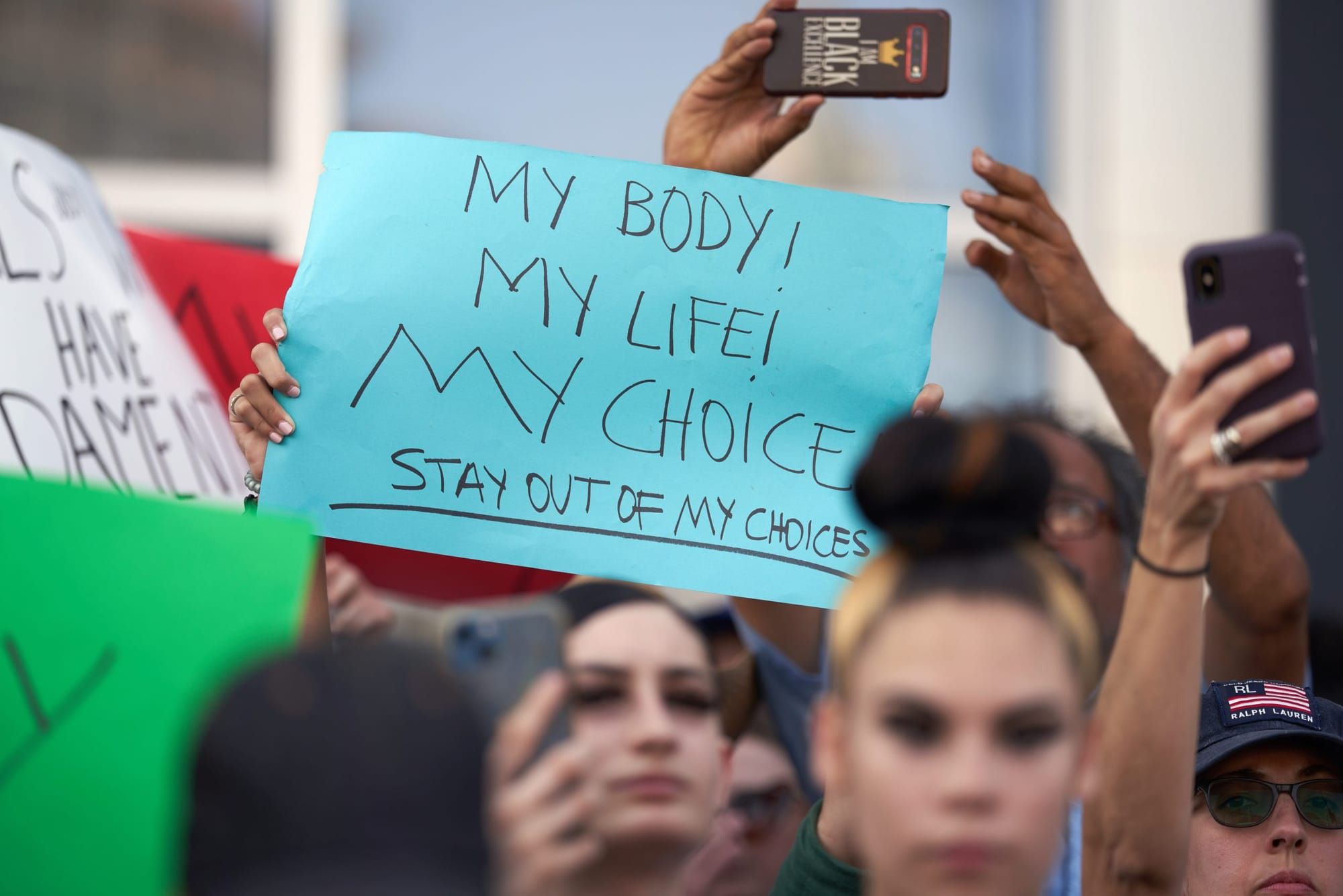 color photograph of an outdoor protest in support of abortion. people's faces in the foreground are blurred, but in the mid-g
