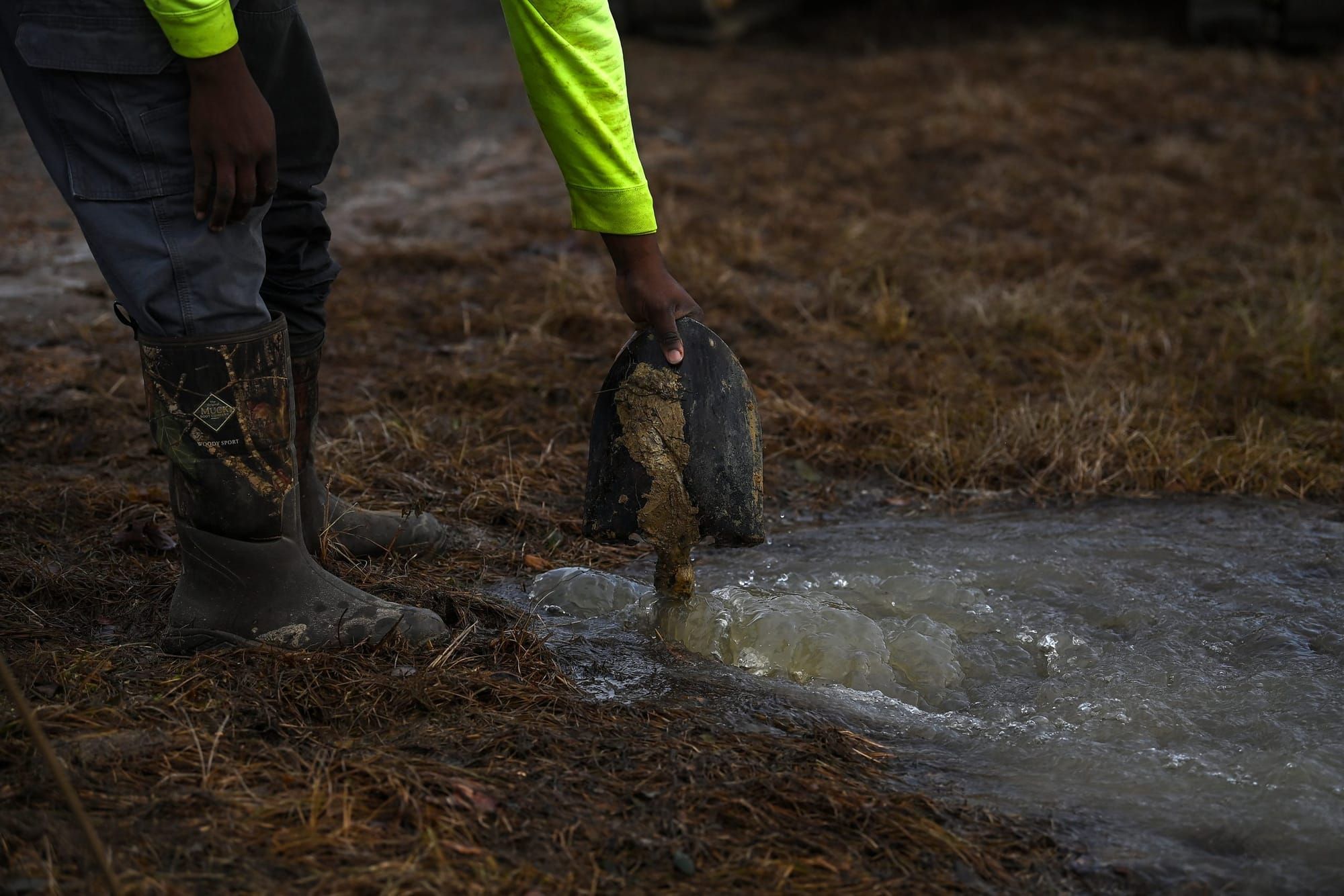 color photograph of a black person's hand holding the head of a shovel sticking out from water