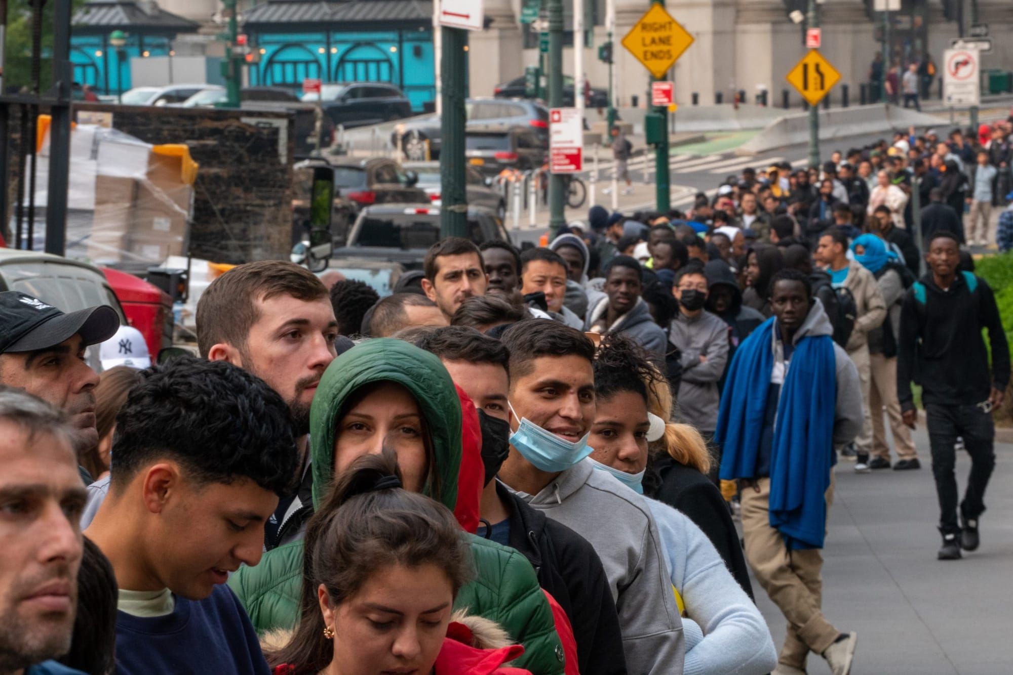color photograph of a line of male asylum-seekers on a New York City sidewalk