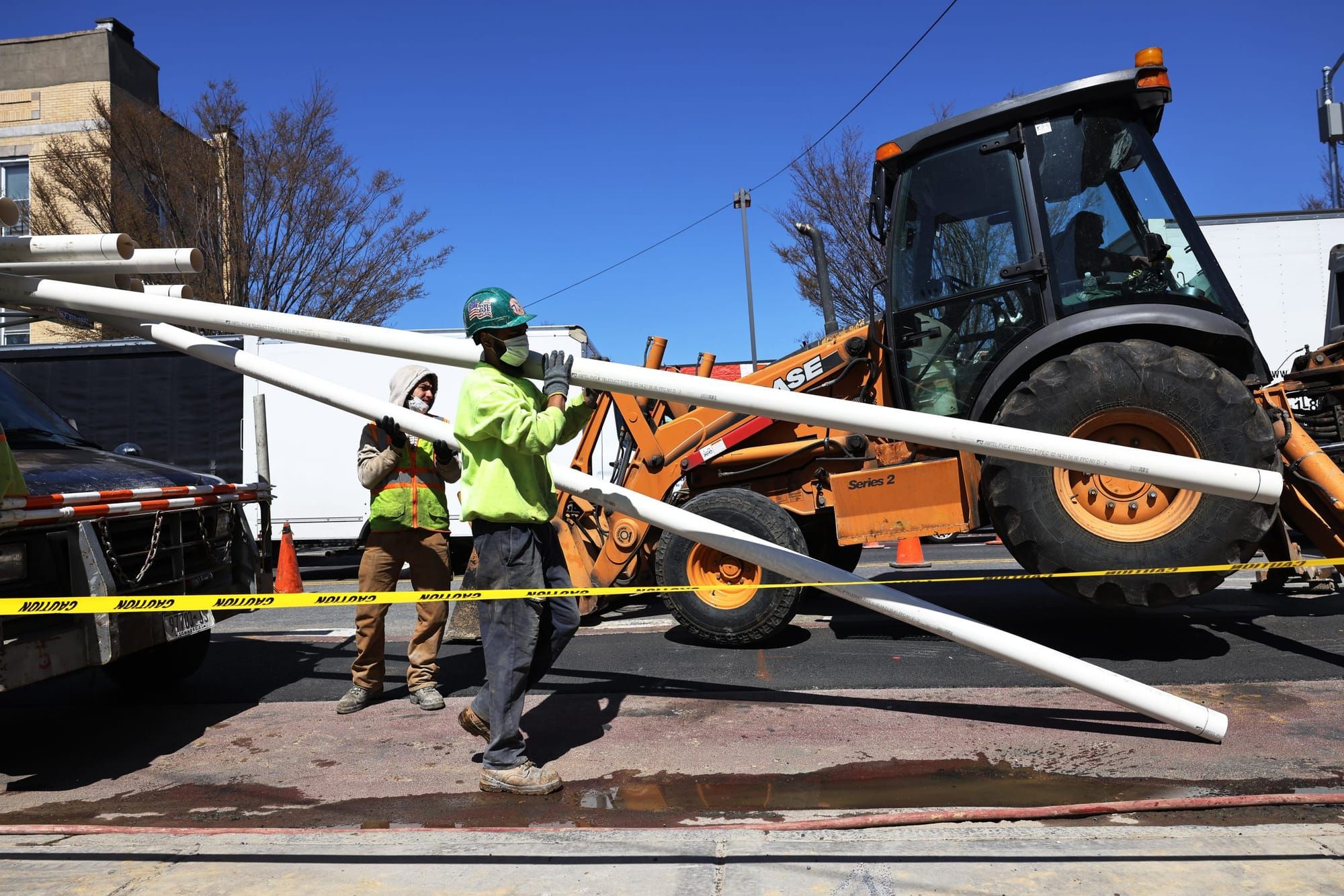 color photograph of a construction worker wearing a bright yellow vest holding a long white pipe