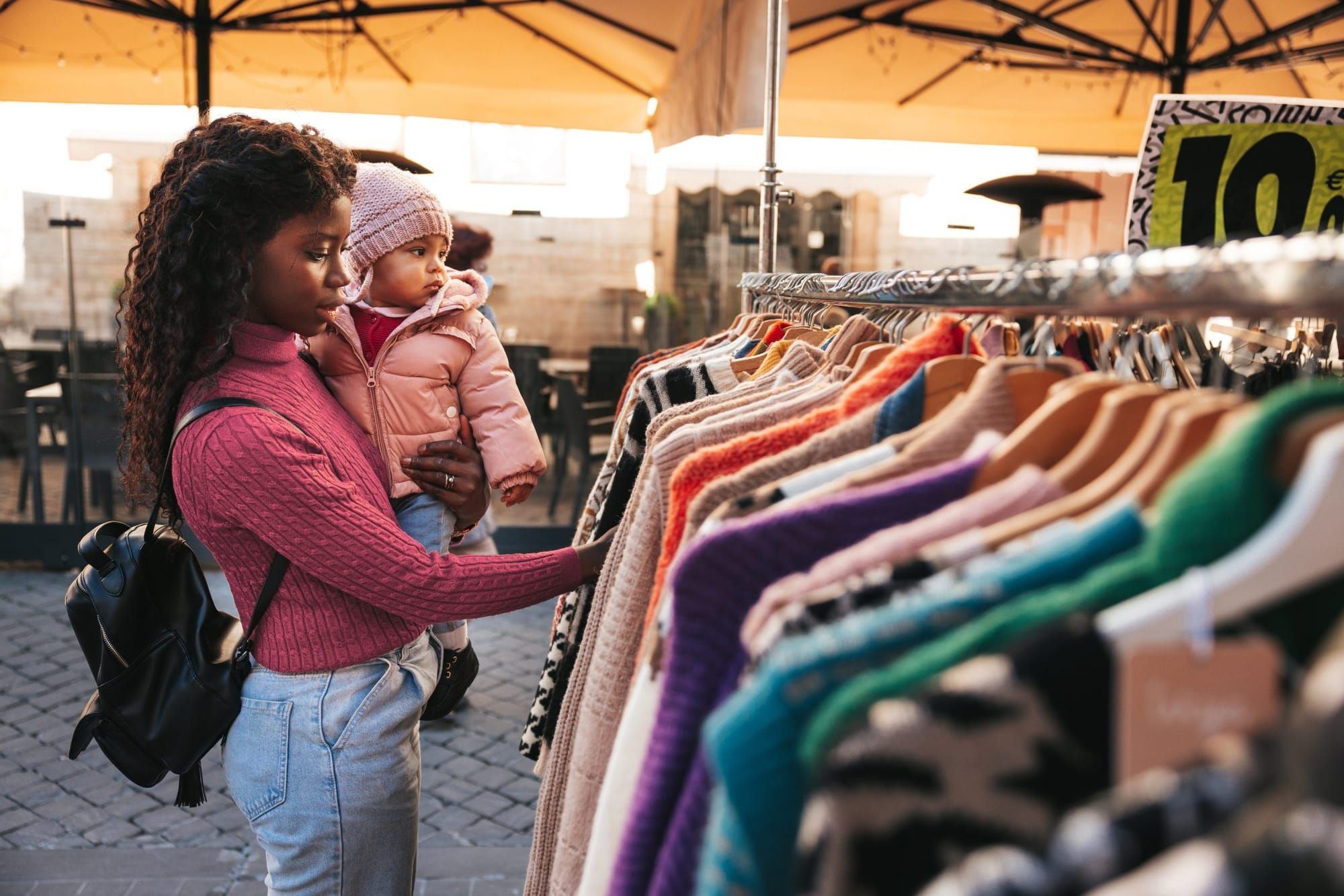 color photograph of a young Black mom wearing a pink turtleneck knitted sweater and lightwash jeans holds a baby in a small p