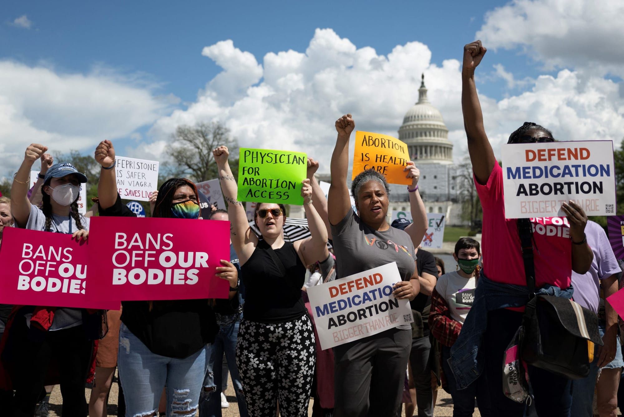 color photograph of an outdoor protest. women of varying racial backgrounds and ages hold signs in support of medication abor
