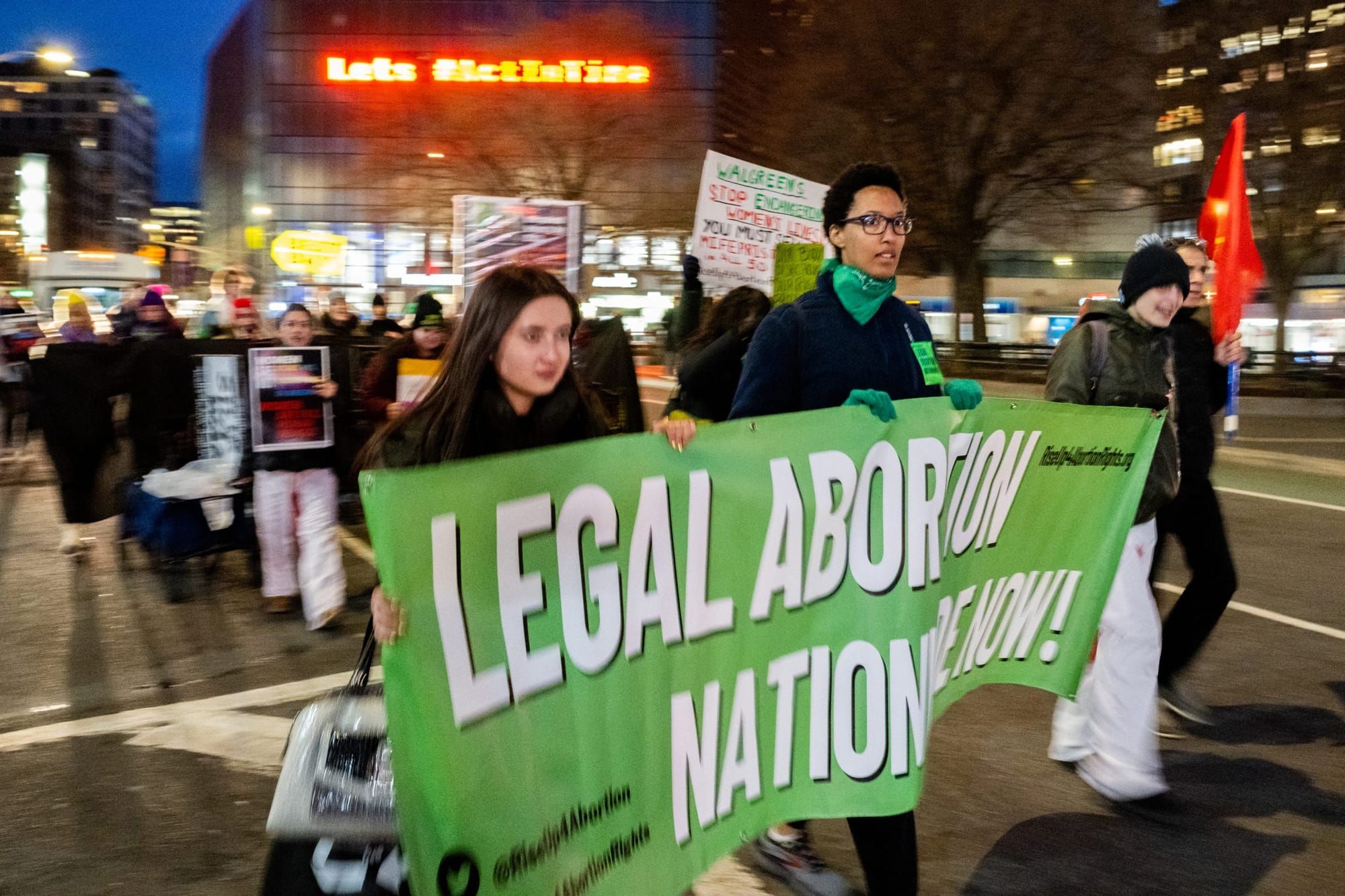color photograph of an outdoor protest in support of abortion rights. two people hold a large green banner with white text th