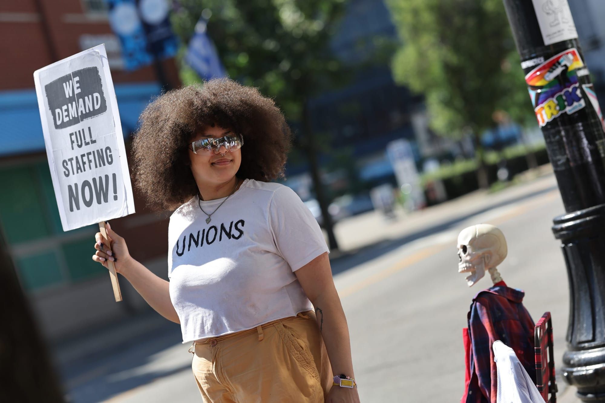 color photograph of a black woman with natural hair at an outdoor protest. she wears a white t-shirt that says "union" in bla