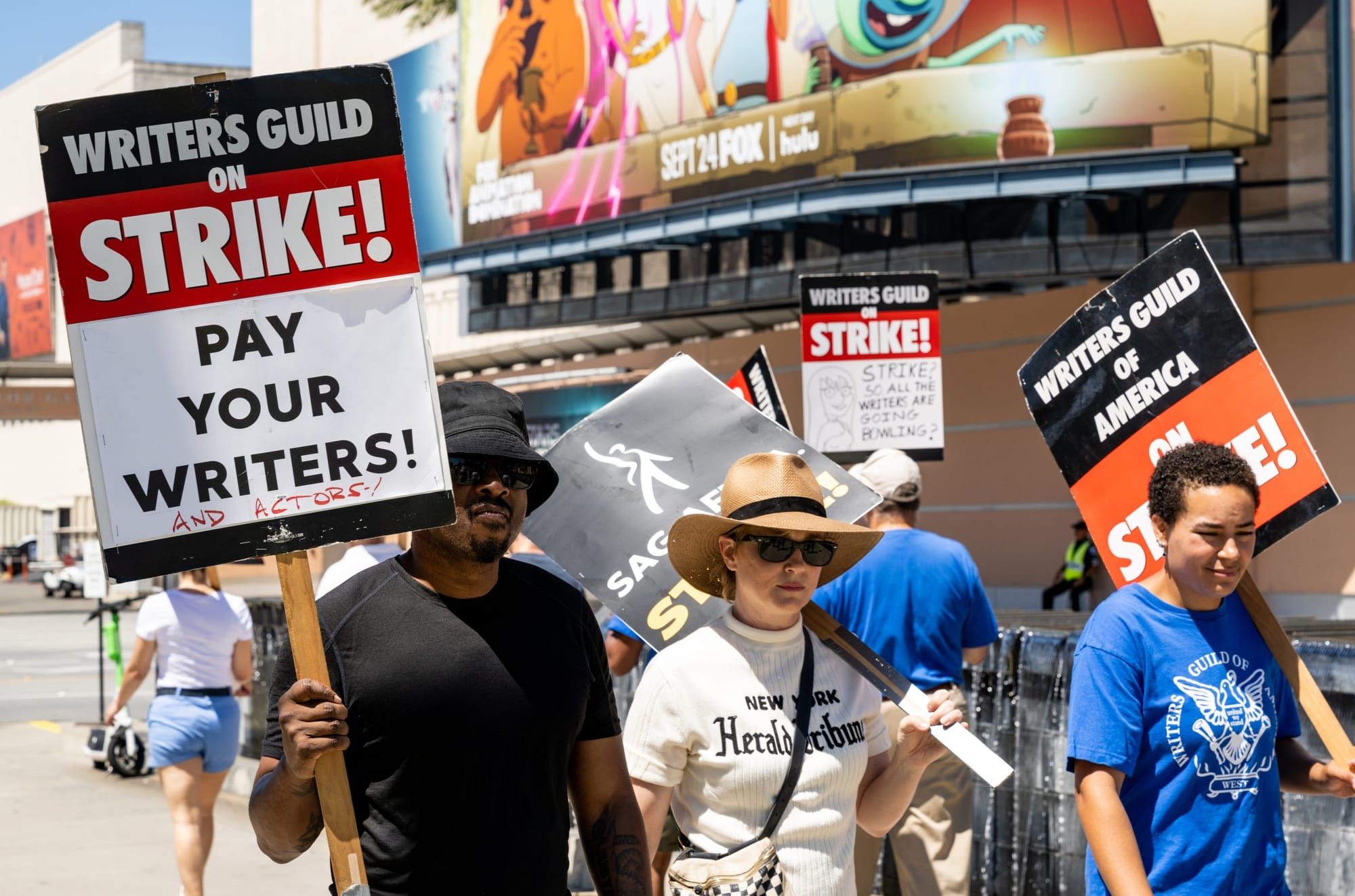 color photograph of an outdoor protest in favor of the Writers Guild of America. three people stand in the foreground with se