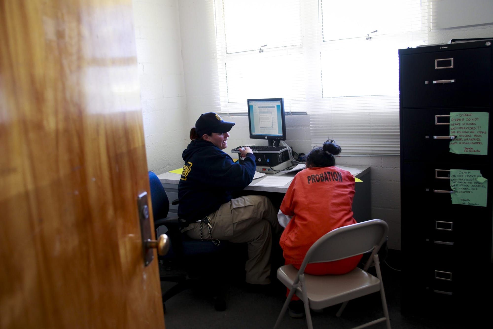color photograph of a young girl in an orange jumpsuit with black text that reads "probation" across the shoulder blades. she