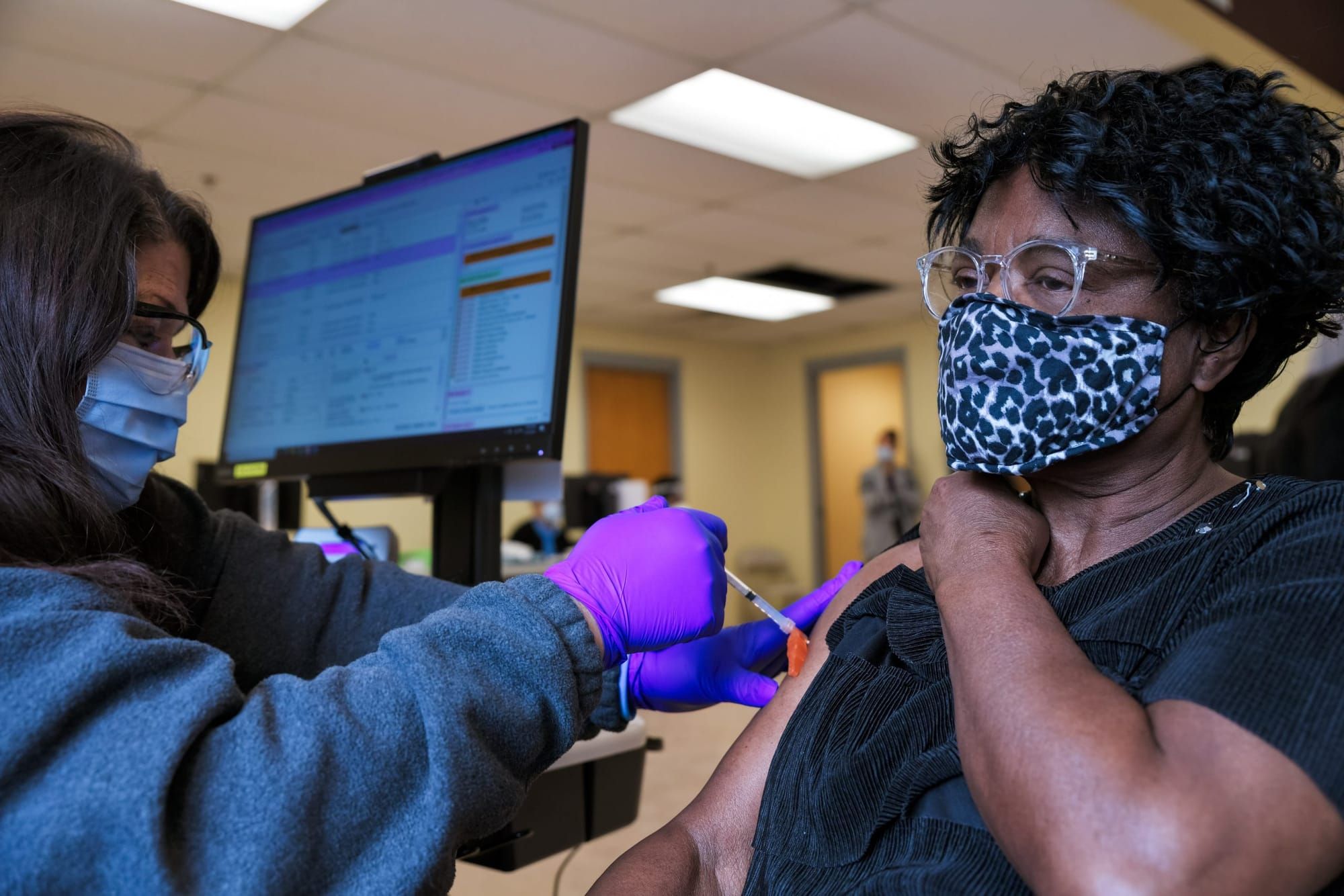 color photograph of a Black woman wearing a cloth mask and pulling up the sleeve of her black t-shirt. a health care worker s