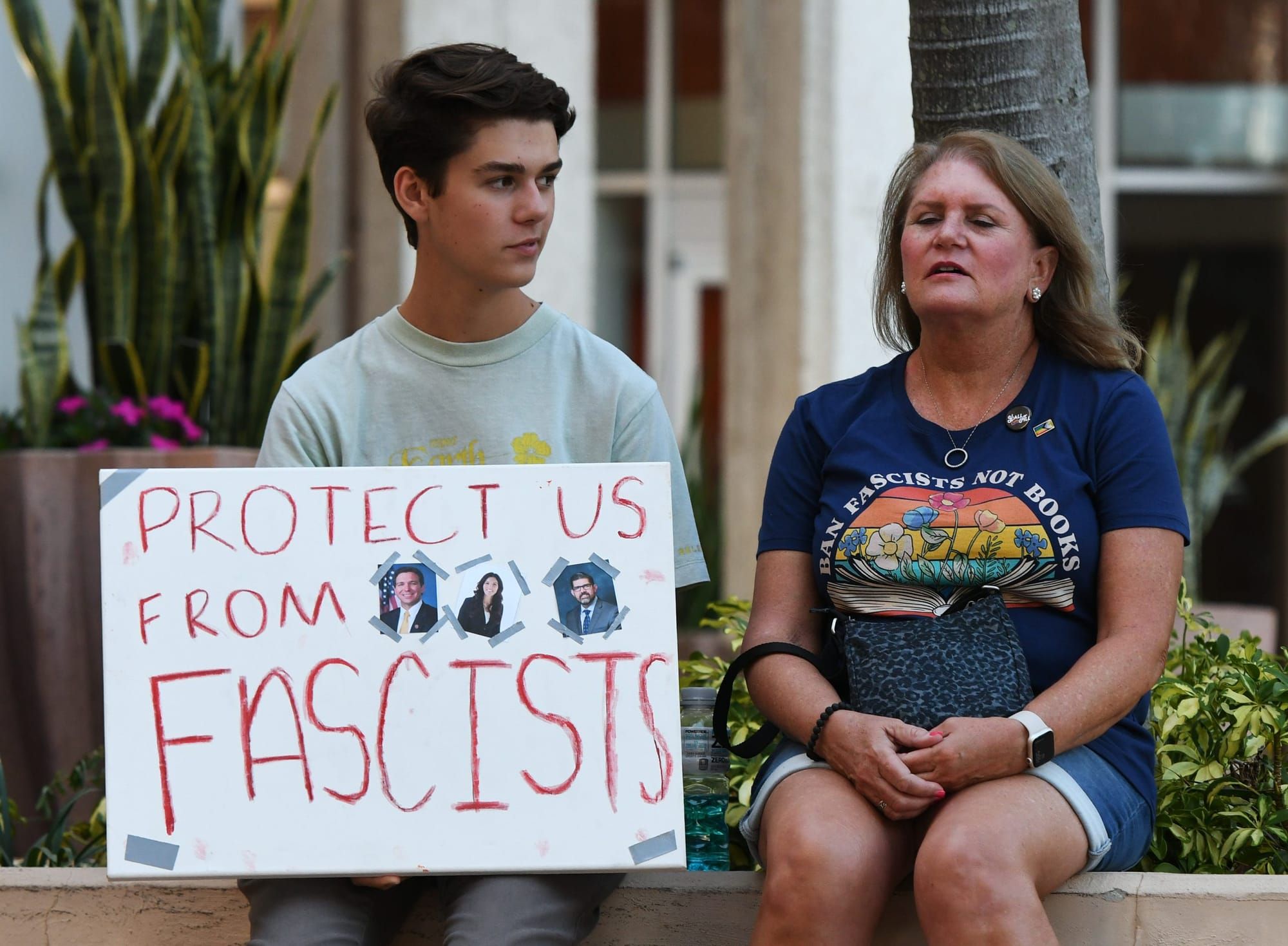 color photograph of a young person sitting on a low stone wall next to a middle-aged woman wearing a dark blue t-shirt that r