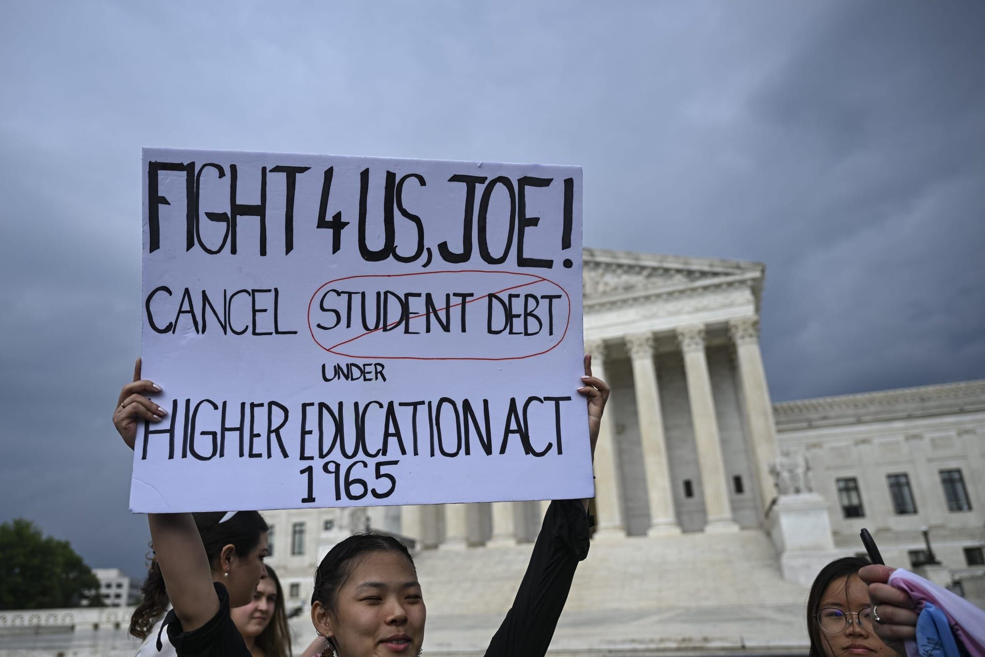 color photograph of a protest outside the Supreme Court building in Washington, D.C. an Asian person holds up a white paper s