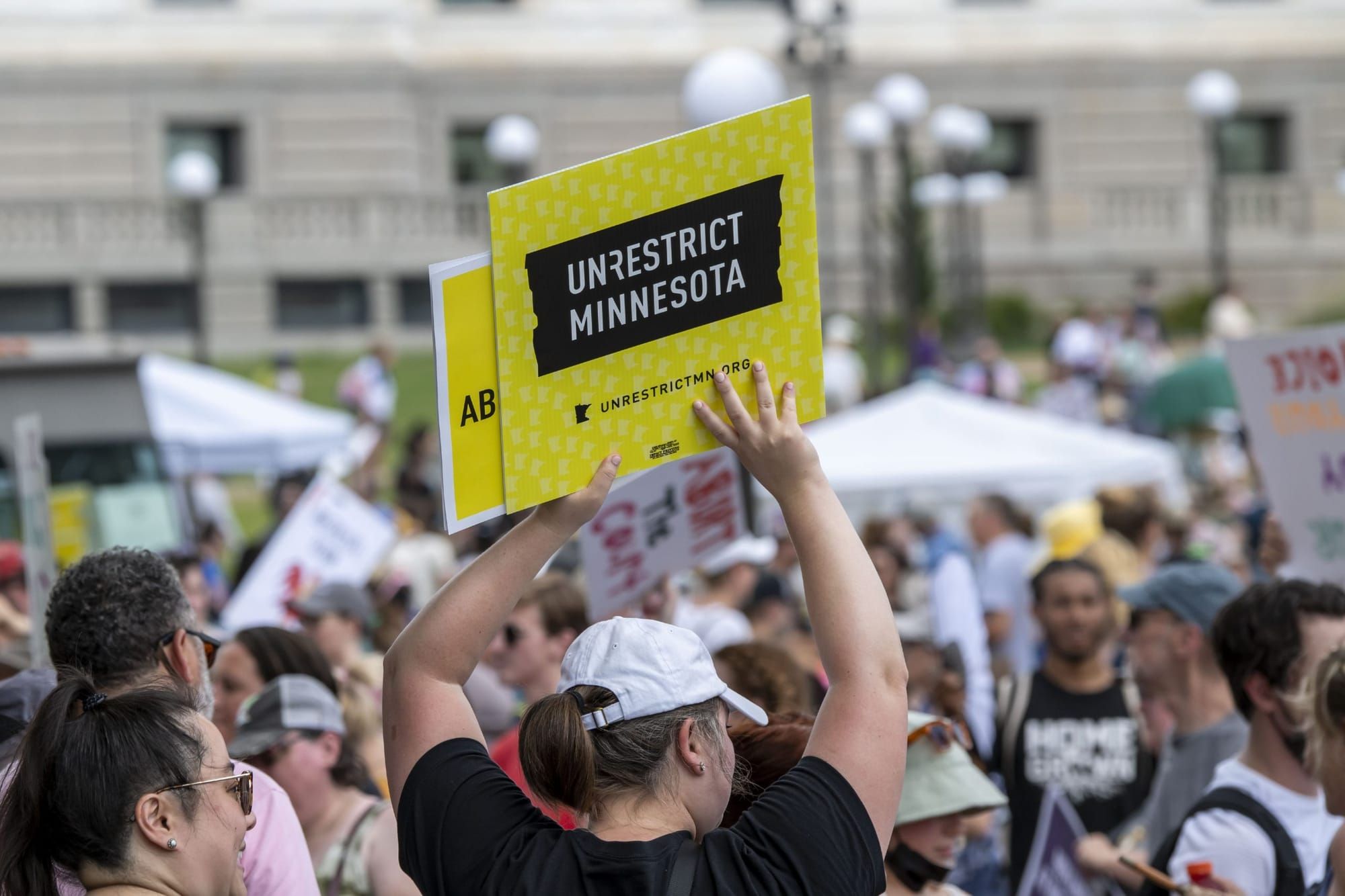 color photograph of an outdoor protest. dozens of people stand in the mid-ground and background. in the foreground, a person