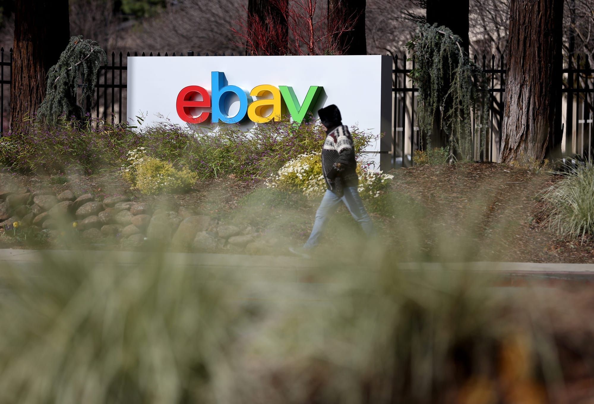 color photograph of a worker walking in the mid-distance in front of a large sign with the ebay logo. the letters are all low