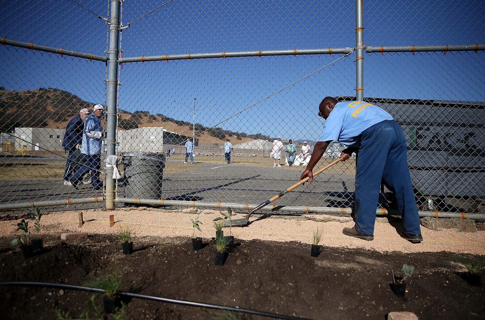 color photograph of an incarcerated person wearing dark blue long pants and a light blue t-shirt with yellow text on the uppe