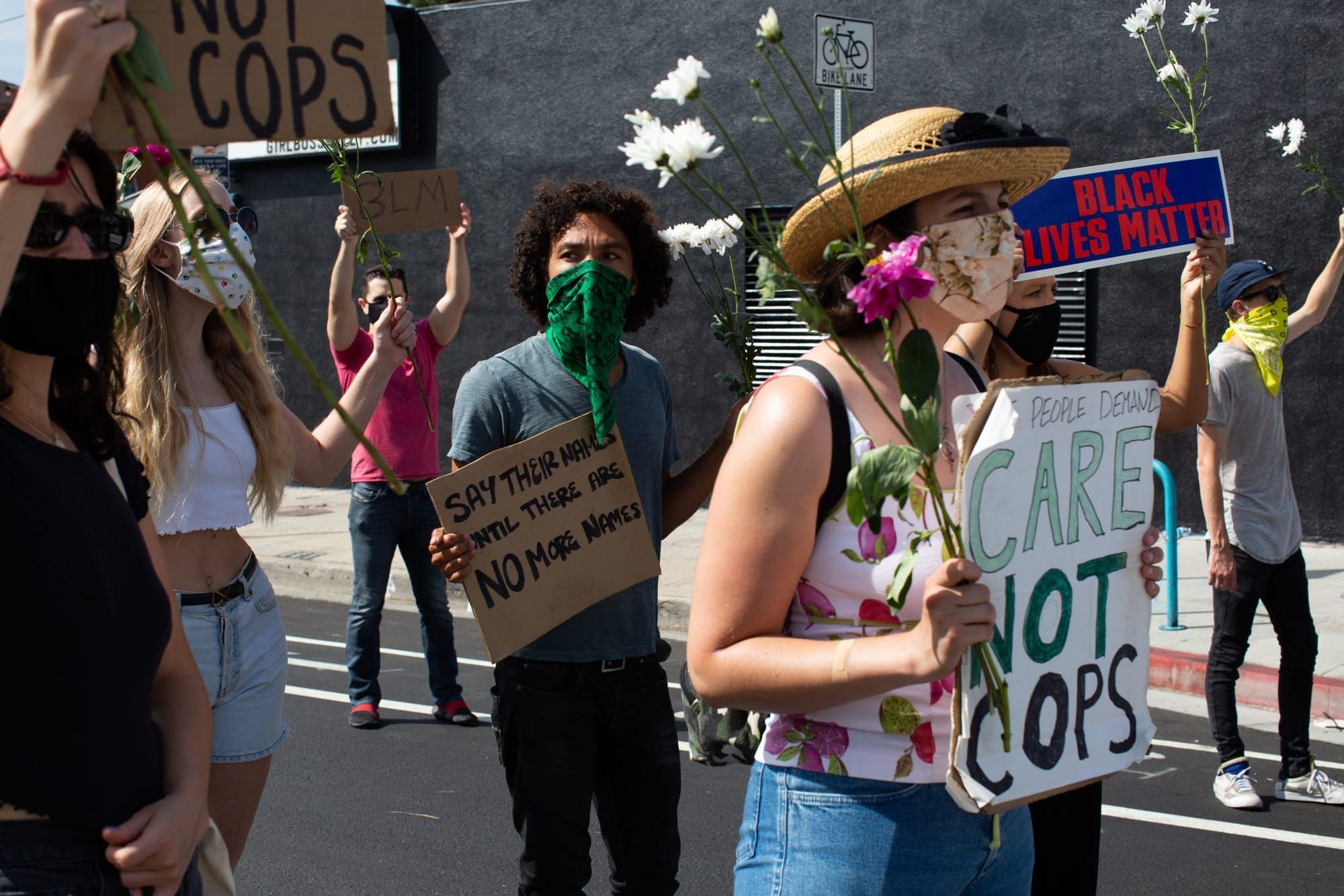 color photograph of an outdoor protest against the police. people wear masks and hold signs with slogans like "care not cops"