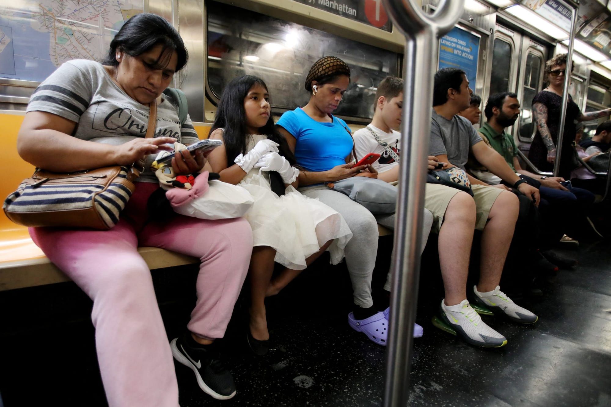 color photograph of Latinx migrants of varying ages, including school-age children, sit on a subway bench