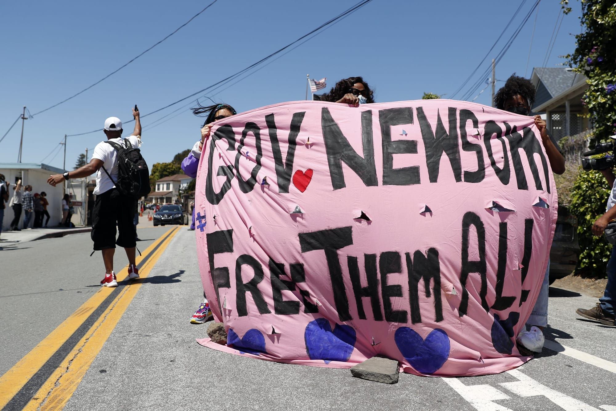 color photograph of an outdoor protest. several people hold up a large pink cloth banner that obscures their bodies. black ha