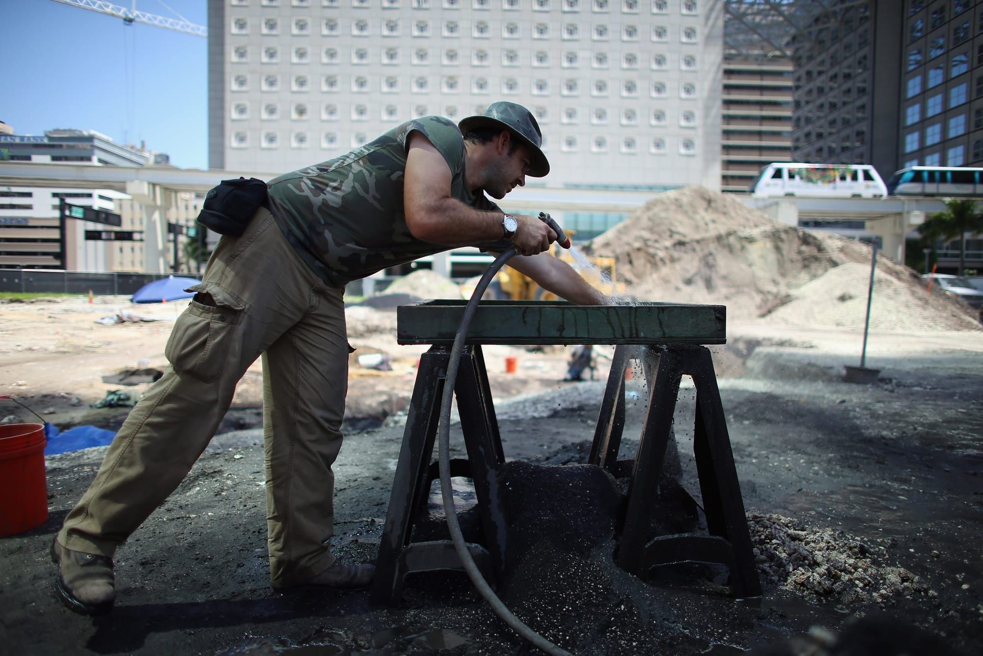 color photograph of an archaeologist leaning over a wooden work station spraying a hose on site