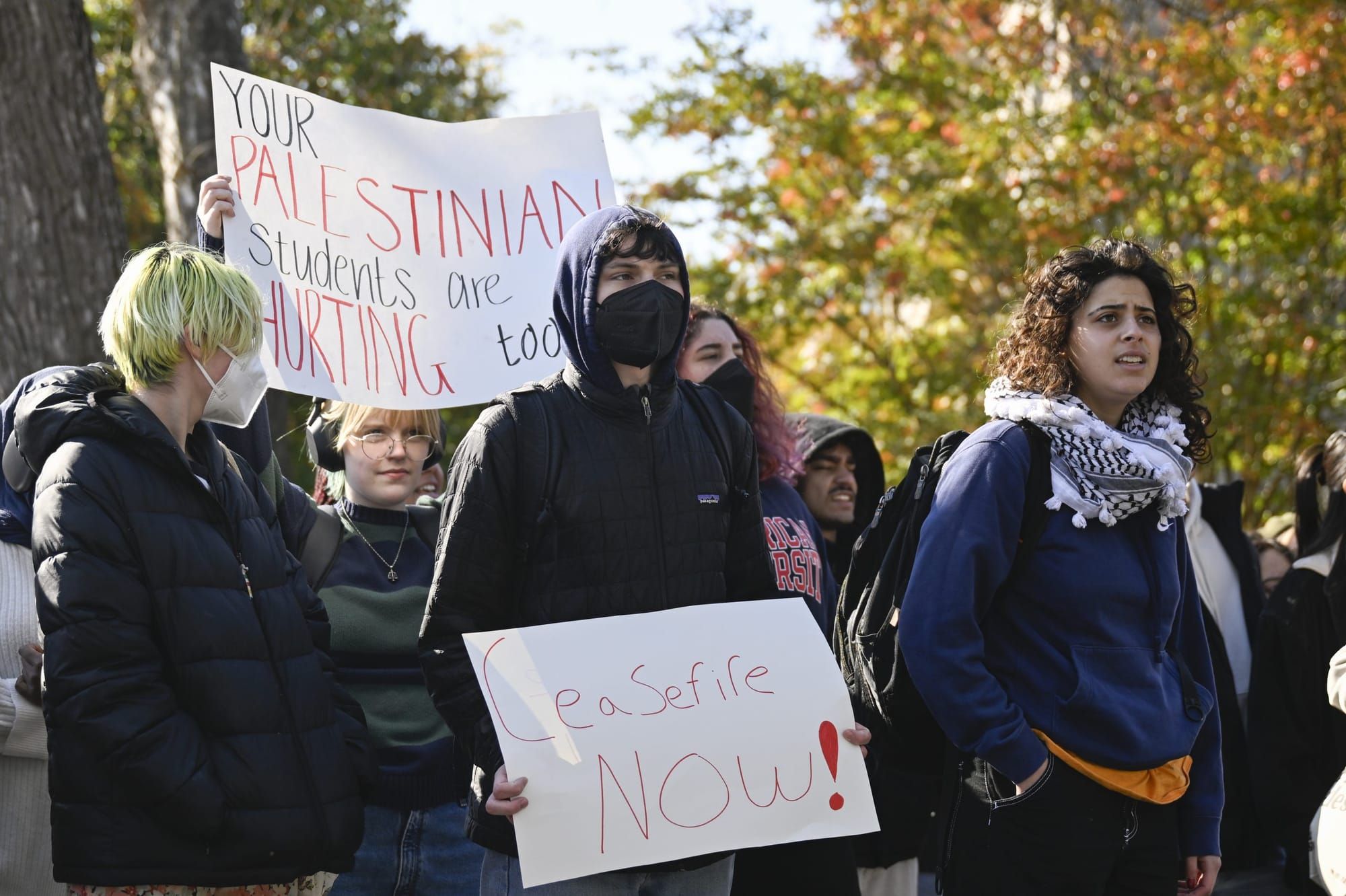 color photograph of an outdoor student protest in support of palestine. students hold white paper posters with handwritten te