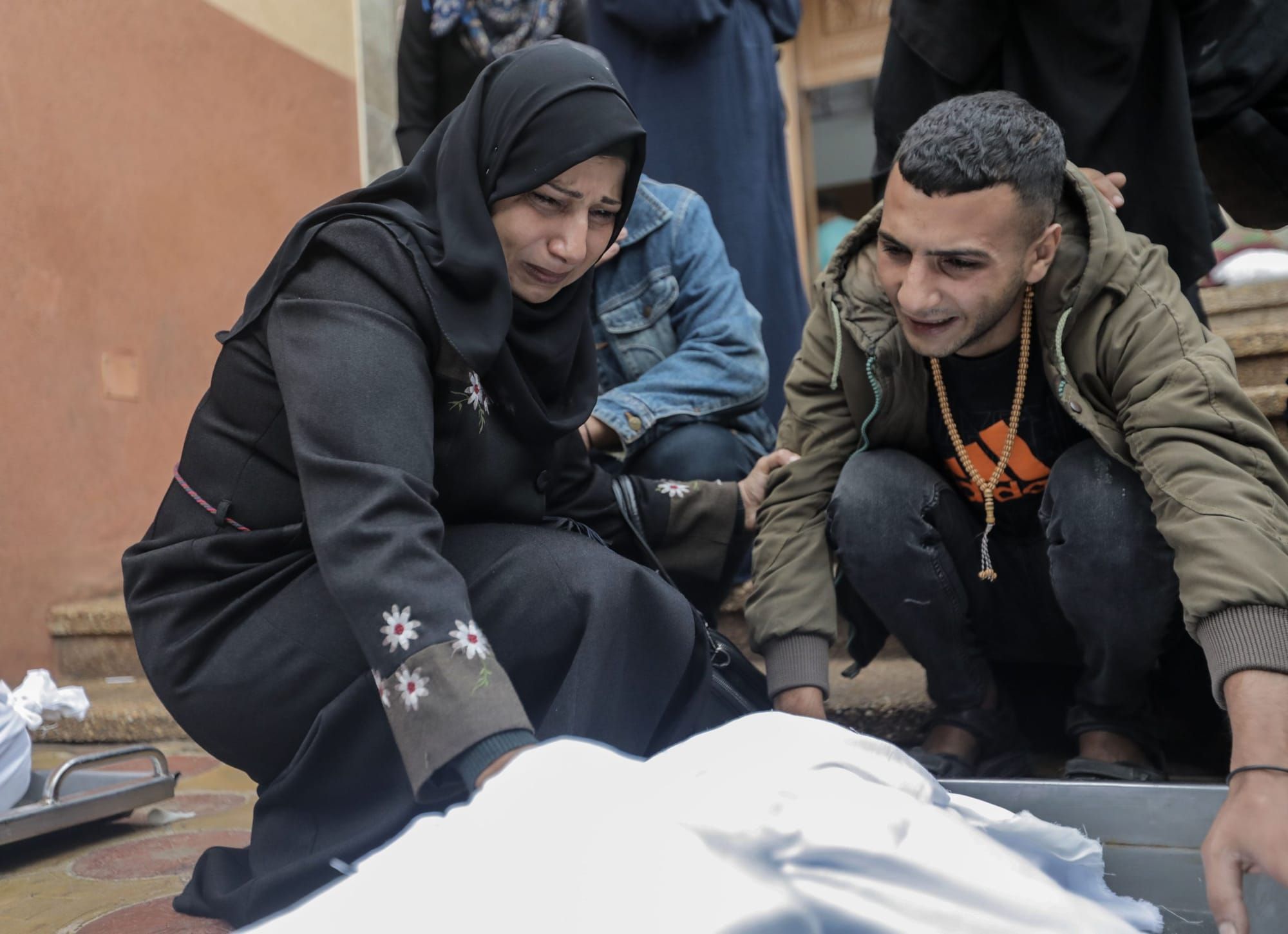color photograph of a Palestinian man and woman crouching over a dead body wrapped in white cloth