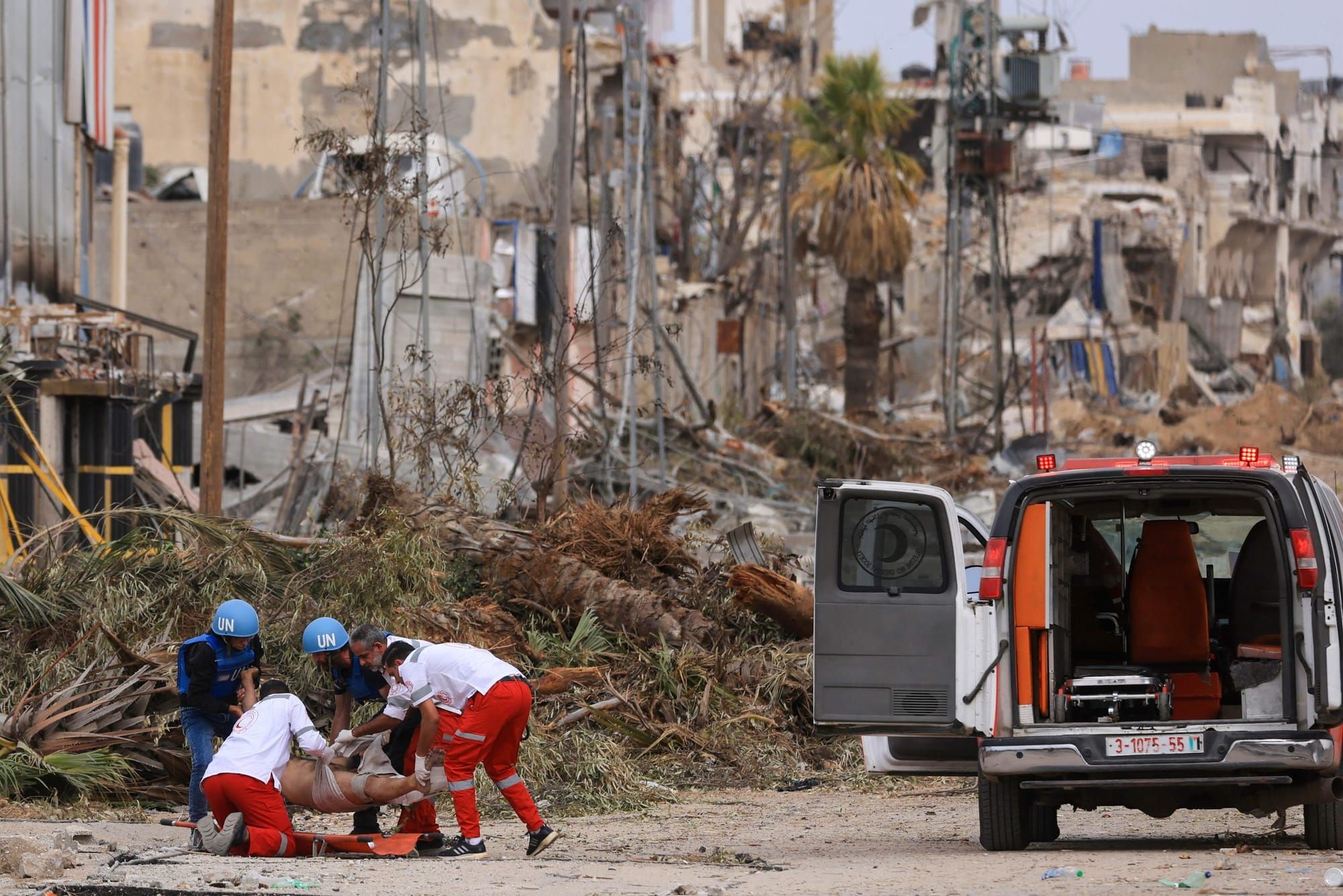 color photograph of a demolished street in Gaza. United Nations medics load a Palestinian man into a van.