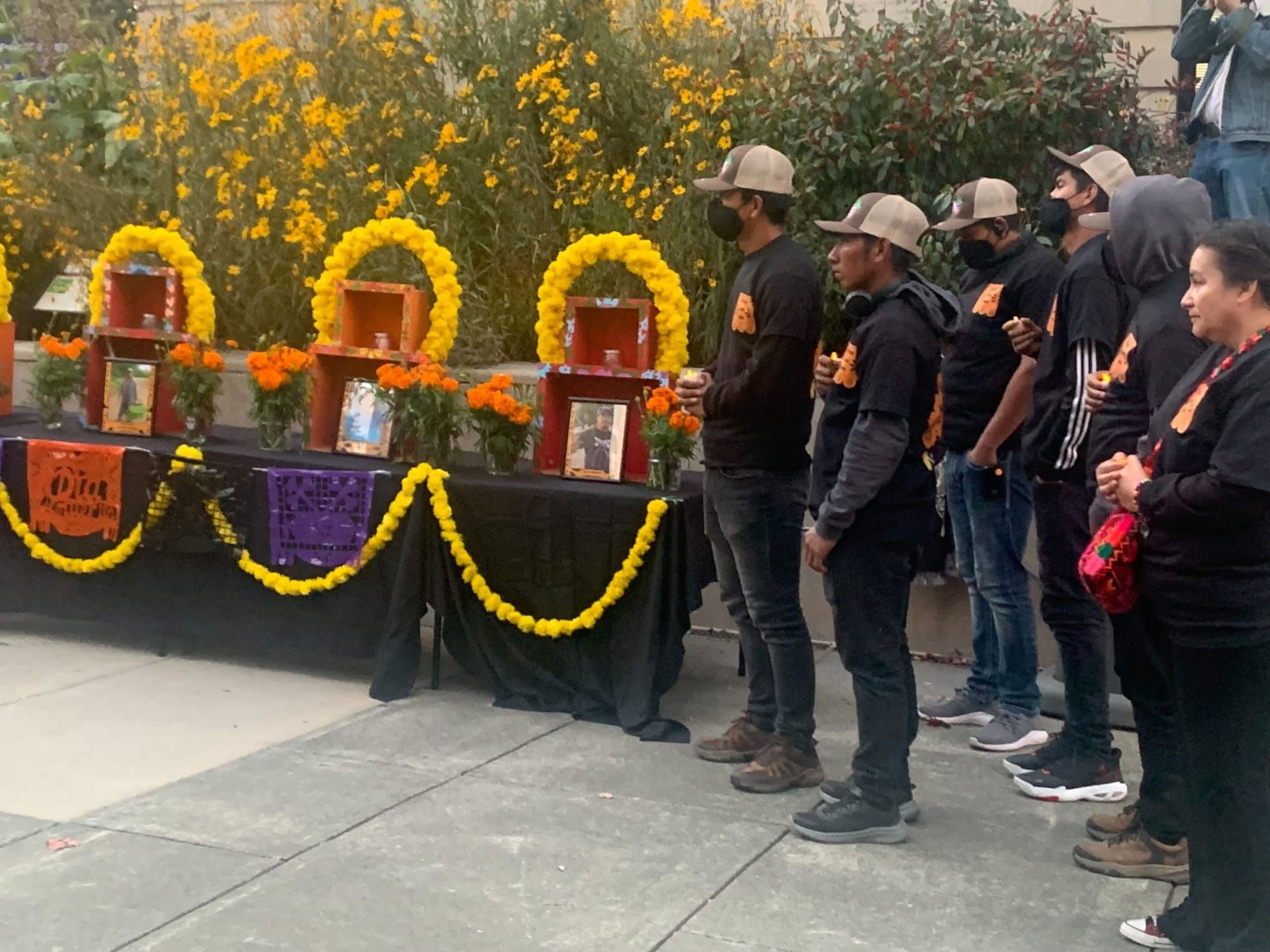 color photograph of about five farmworkers and farmworker advocates wearing dark clothing and face masks standing to the righ