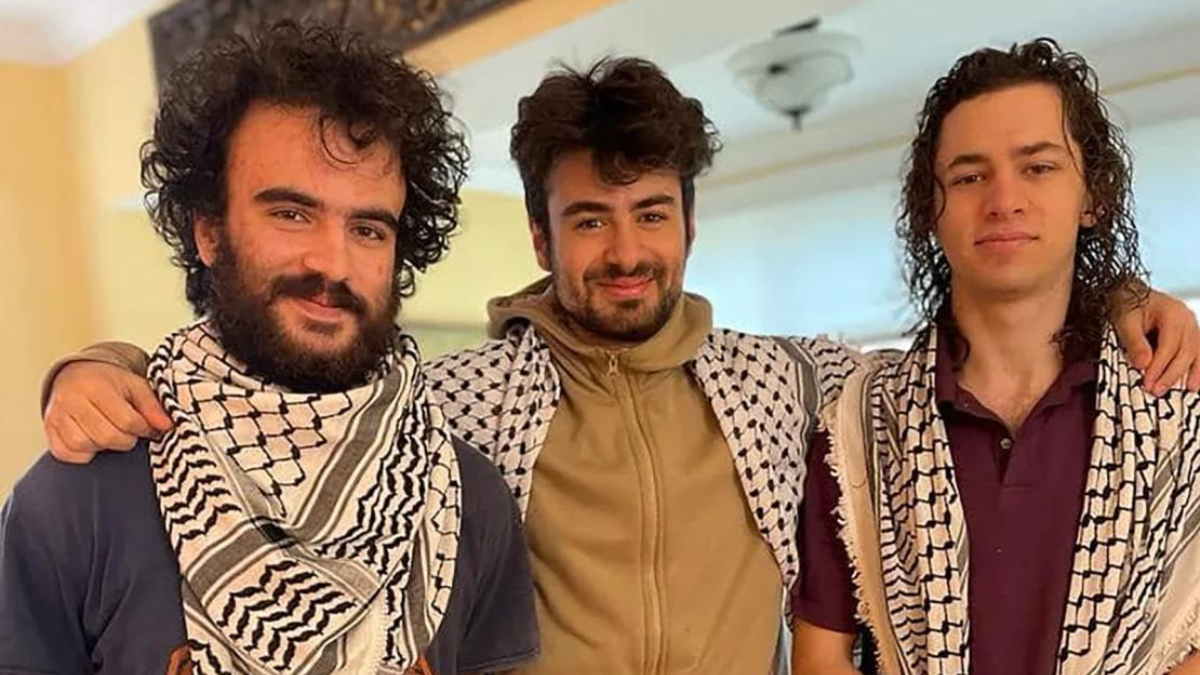 color photograph of three young Palestinian men wearing keffiyehs with their arms around each others' shoulders