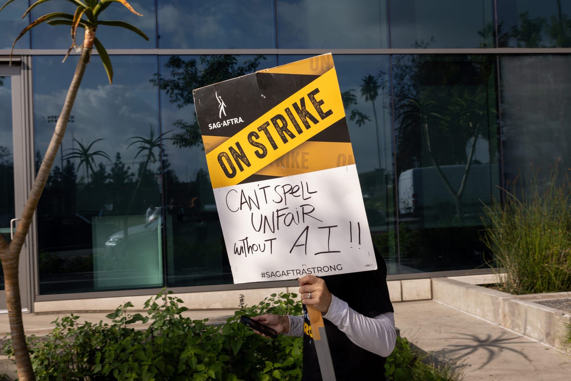 color photograph of someone holding a picket sign in front of their face that reads "SAG-AFTRA on strike" in printed text and