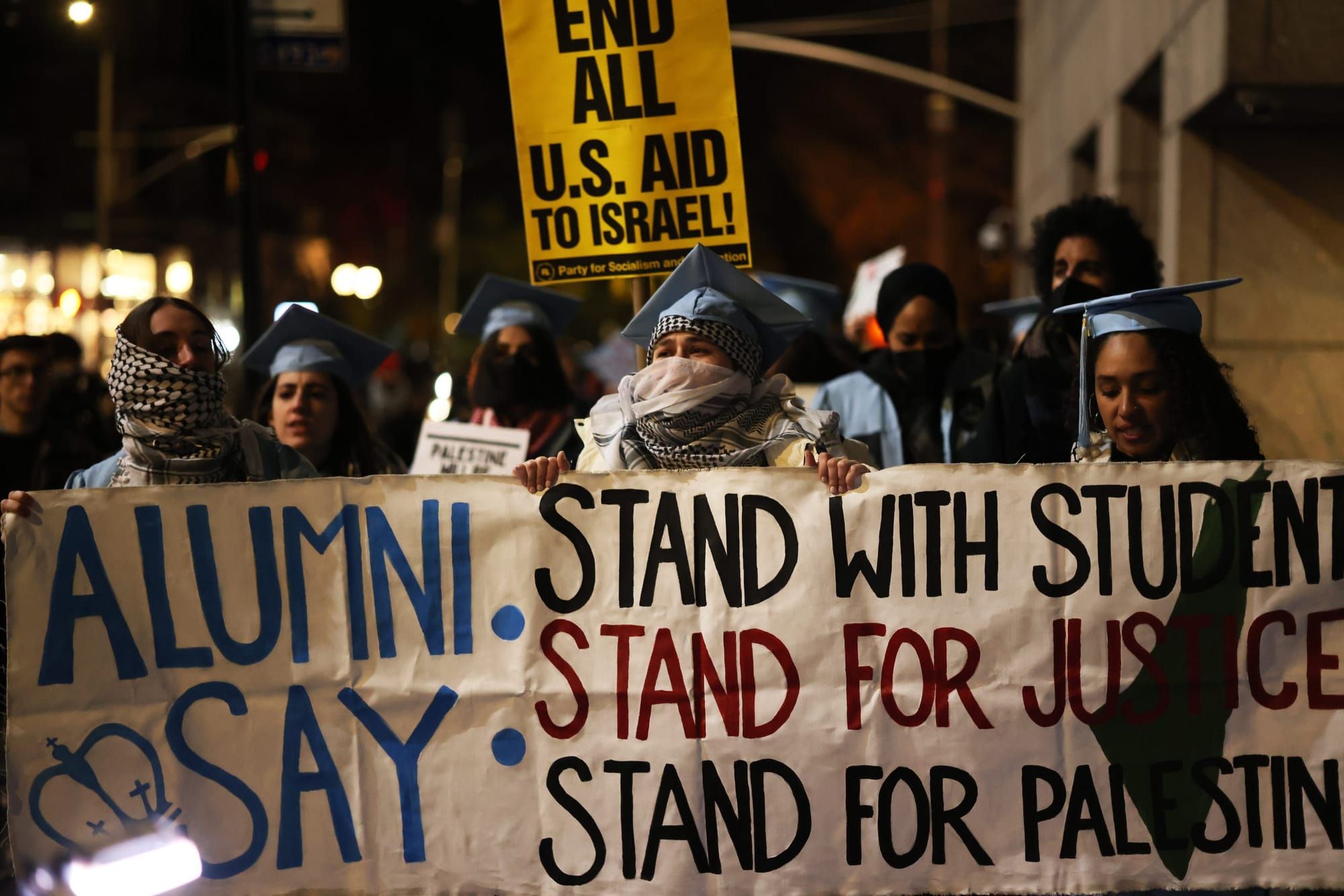 color photograph of an outdoor, nighttime protest by Columbia University alumni in support of Palestinian liberation. several