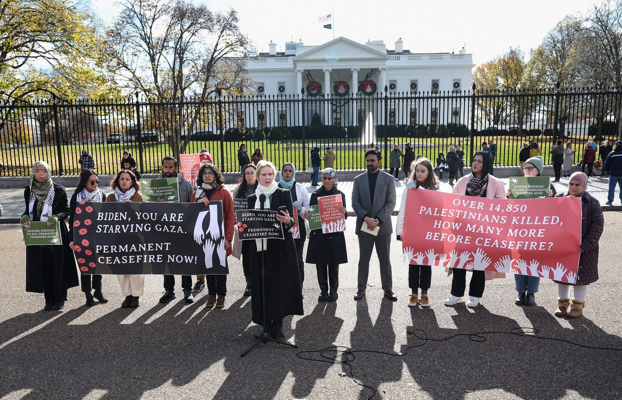 color photograph of an outdoor protest for a ceasefire in gaza in front of the white house gates. people hold large banners w