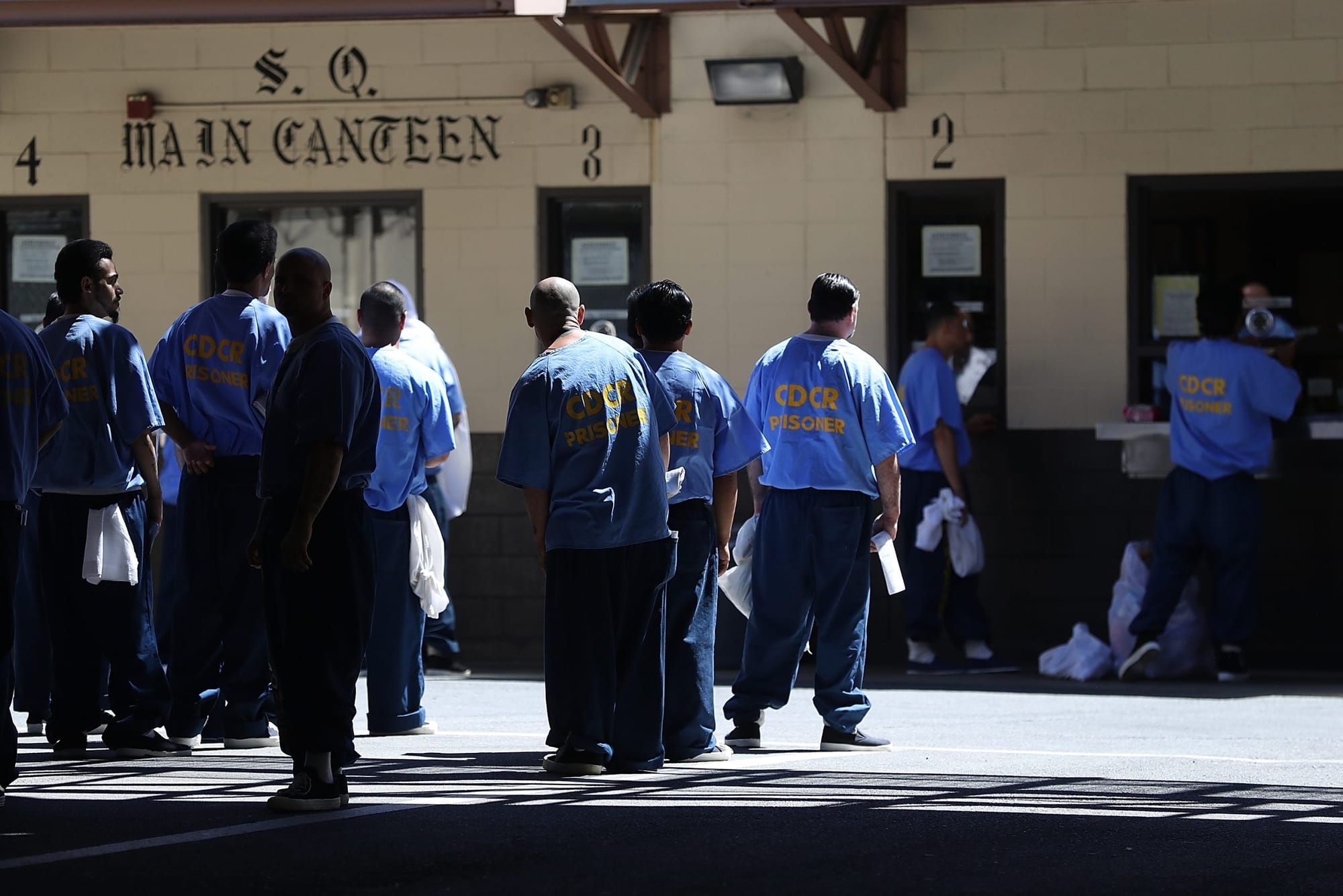 color photograph of incarcerated men wearing light blue Department of Corrections shirts standing outside the canteen in San
